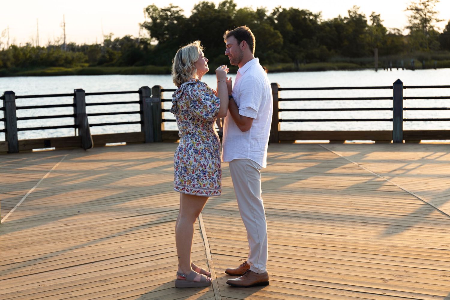 A couple shares a romantic moment during sunset on a wooden boardwalk by the water.