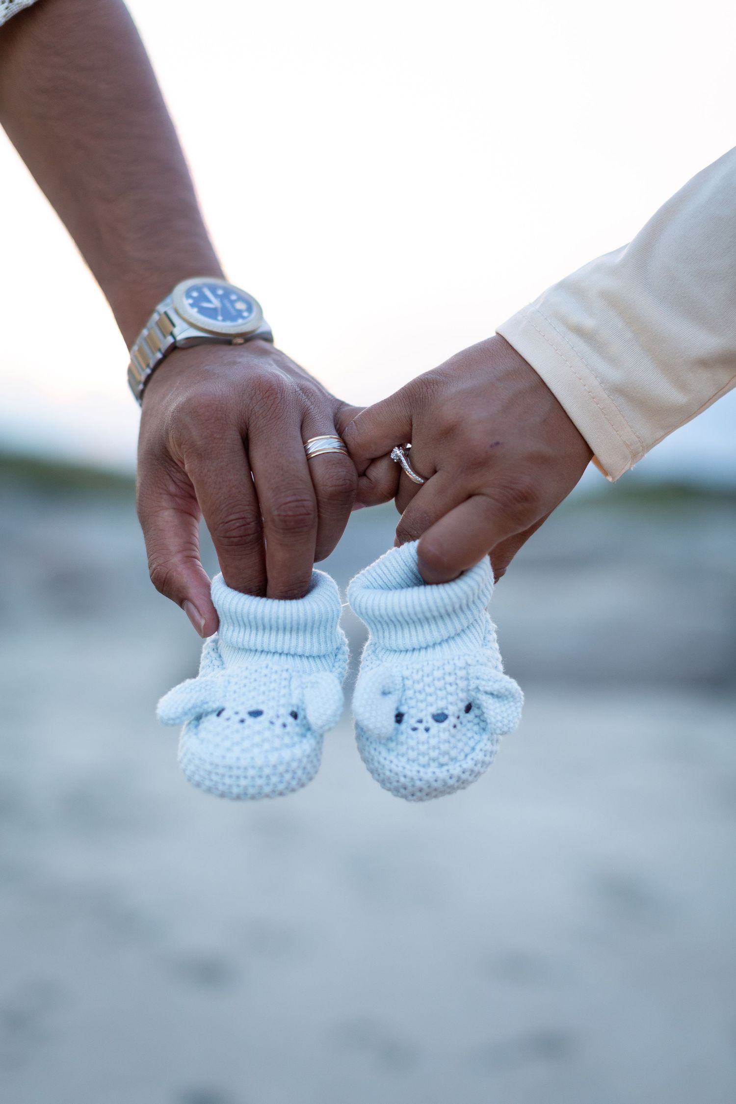 Close-up view of hands holding tiny white knitted baby booties against a soft blurred background.