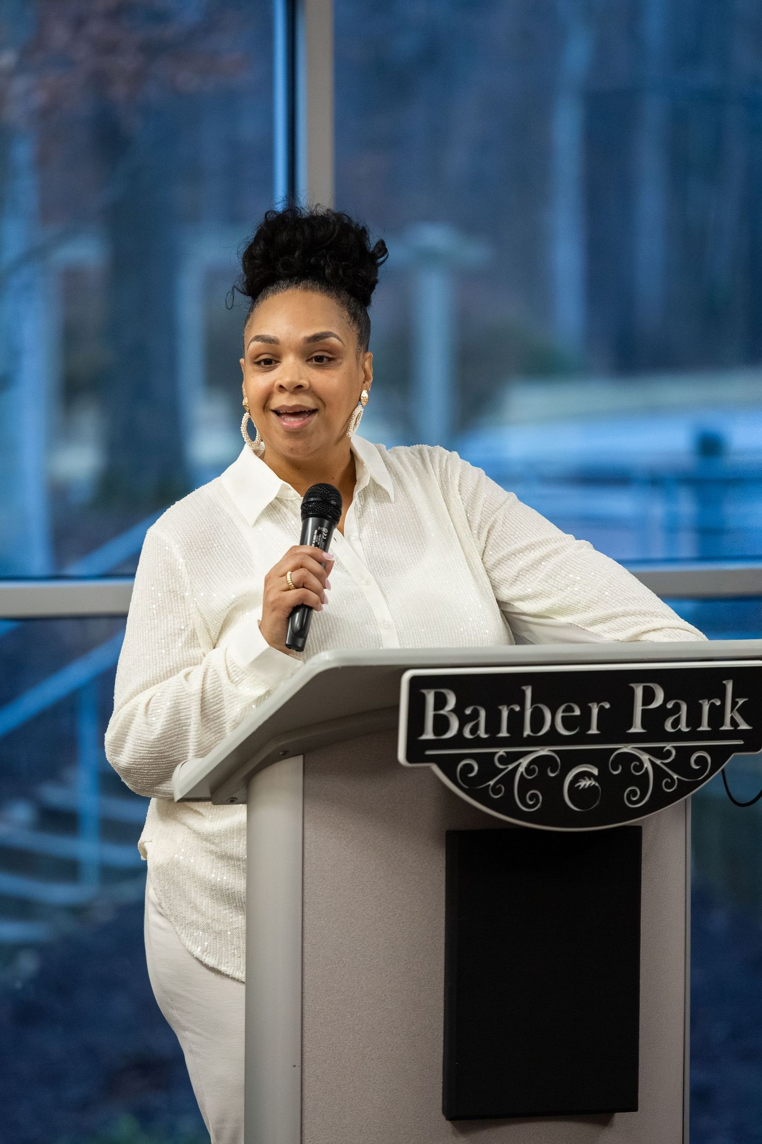 Speaker stands at podium labeled 'Barber Park' during an indoor presentation event.