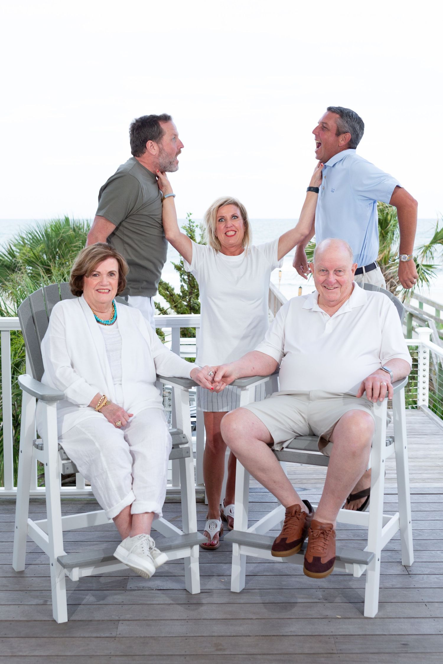 Family members relaxing in white Adirondack chairs on a wooden deck.