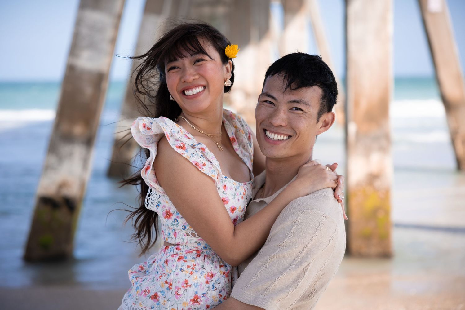 A couple shares a joyful embrace under a pier at the beach.