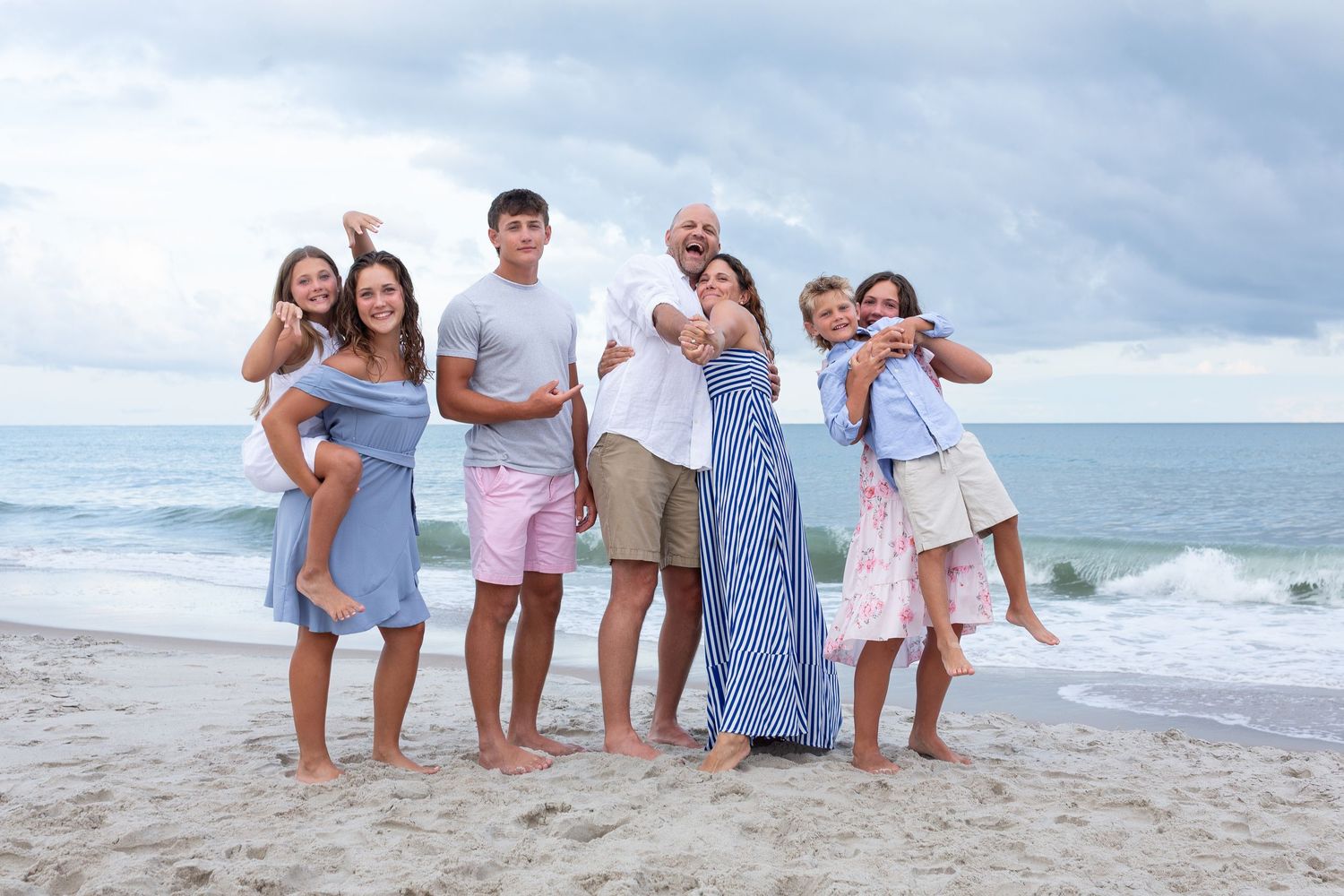 Beachside family photo session with ocean waves and cloudy sky backdrop.