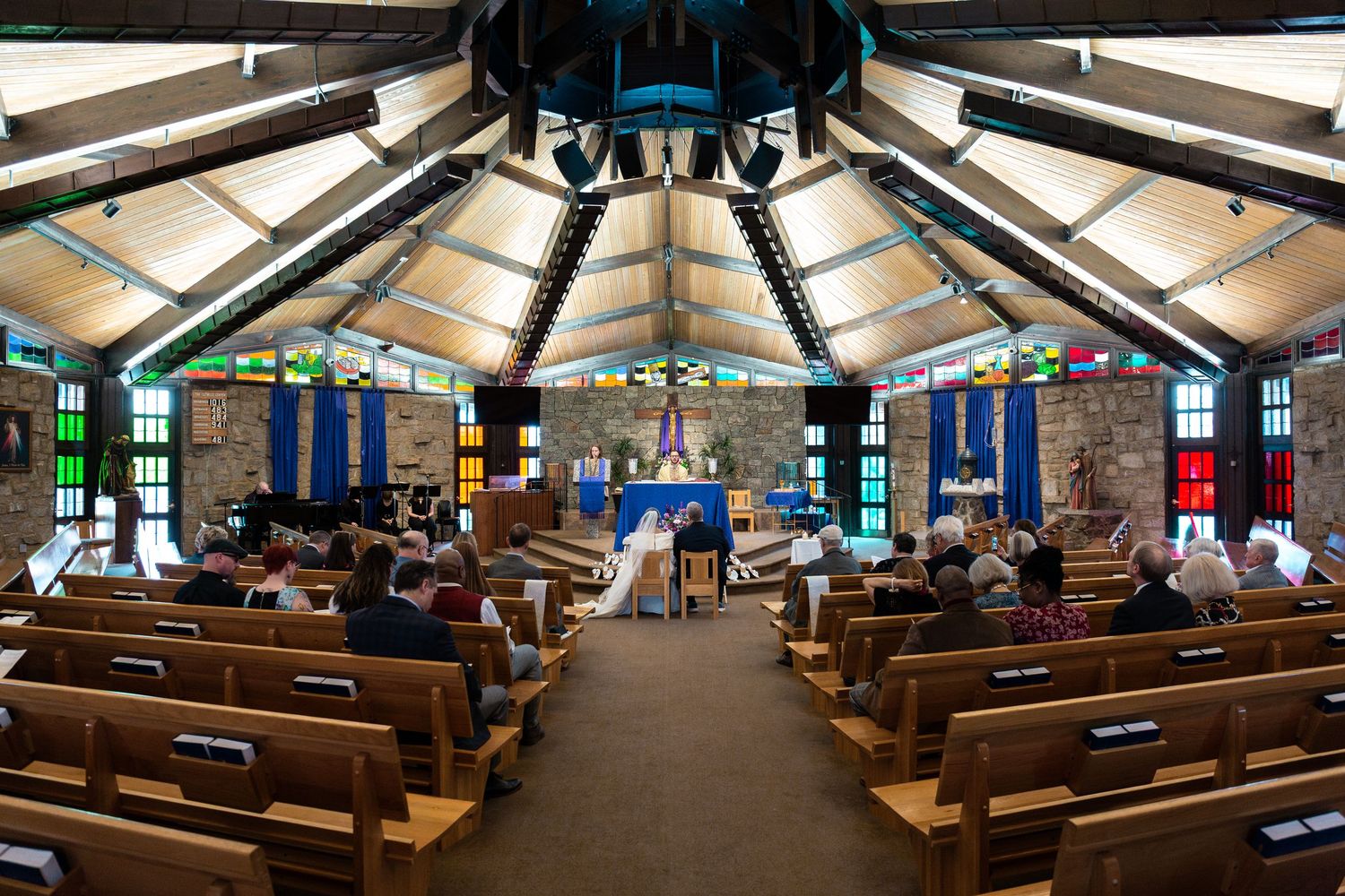 Interior view of a modern octagonal church sanctuary with wooden pews, stone walls and blue banners hanging from the ceiling.