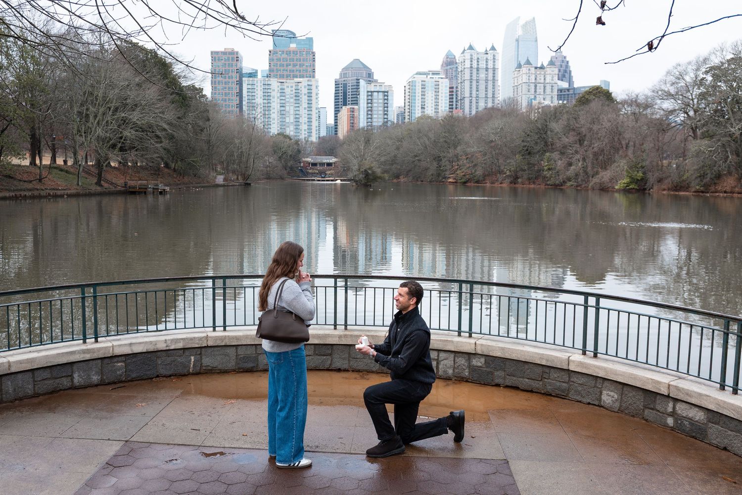 A romantic proposal moment at a scenic overlook in Piedmont Park with the Atlanta skyline and lake in the background.