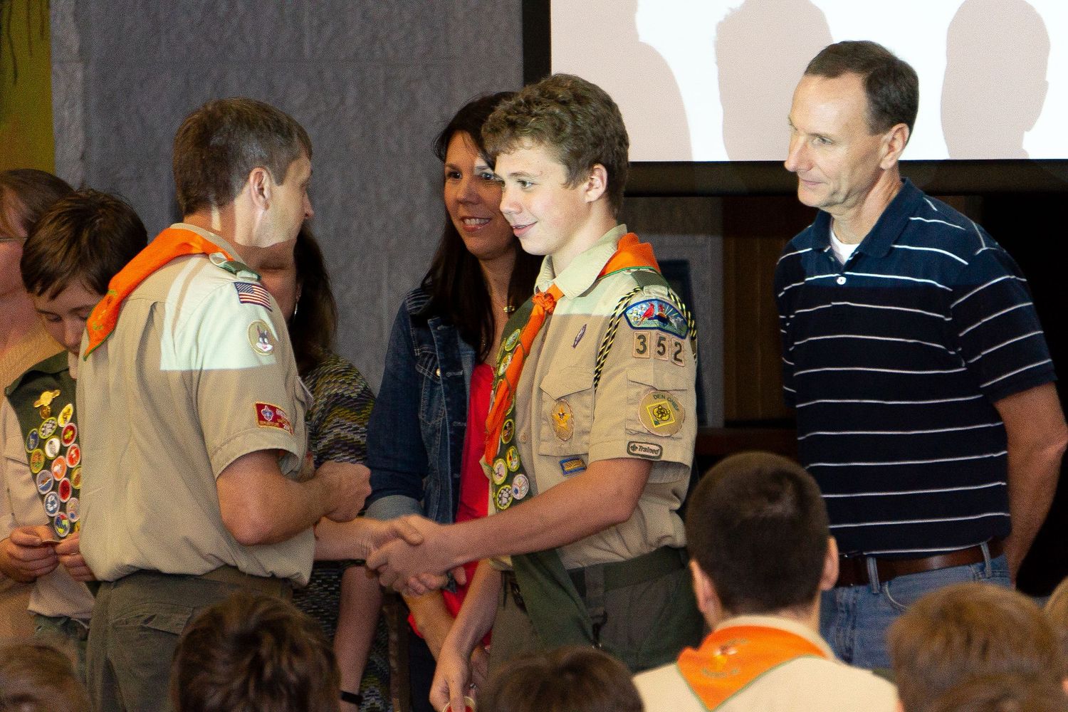 Boy Scout leaders and scouts interact during an award ceremony with people wearing orange and tan uniforms.