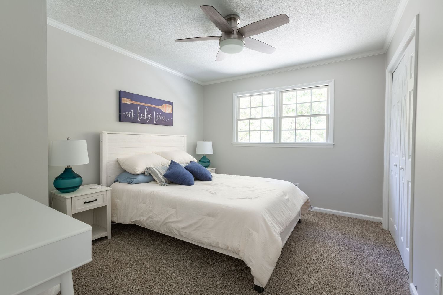 Modern bedroom interior with white walls, ceiling fan, and natural light streaming through window.