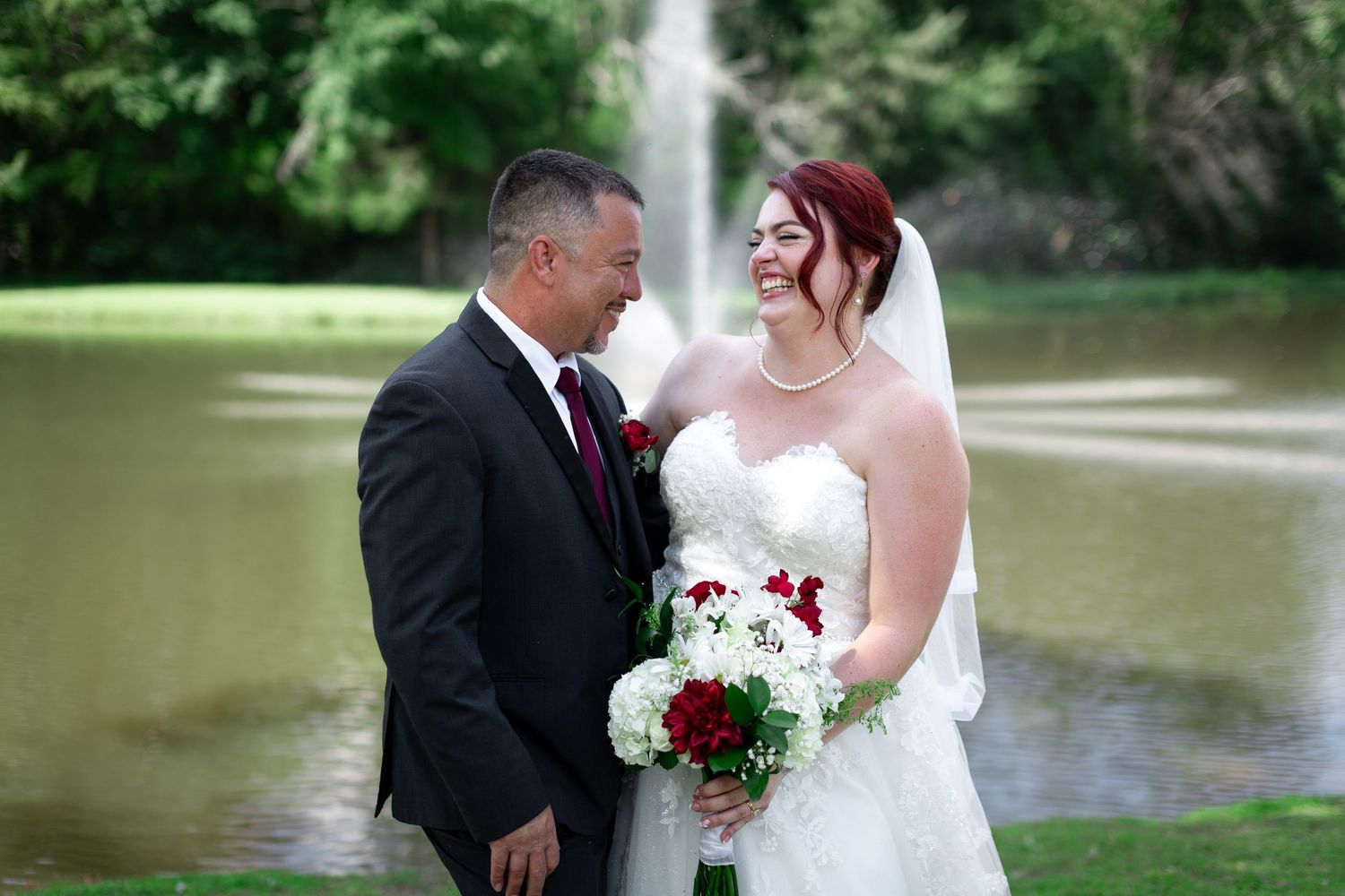 A romantic wedding couple embraces near a serene pond surrounded by lush greenery.