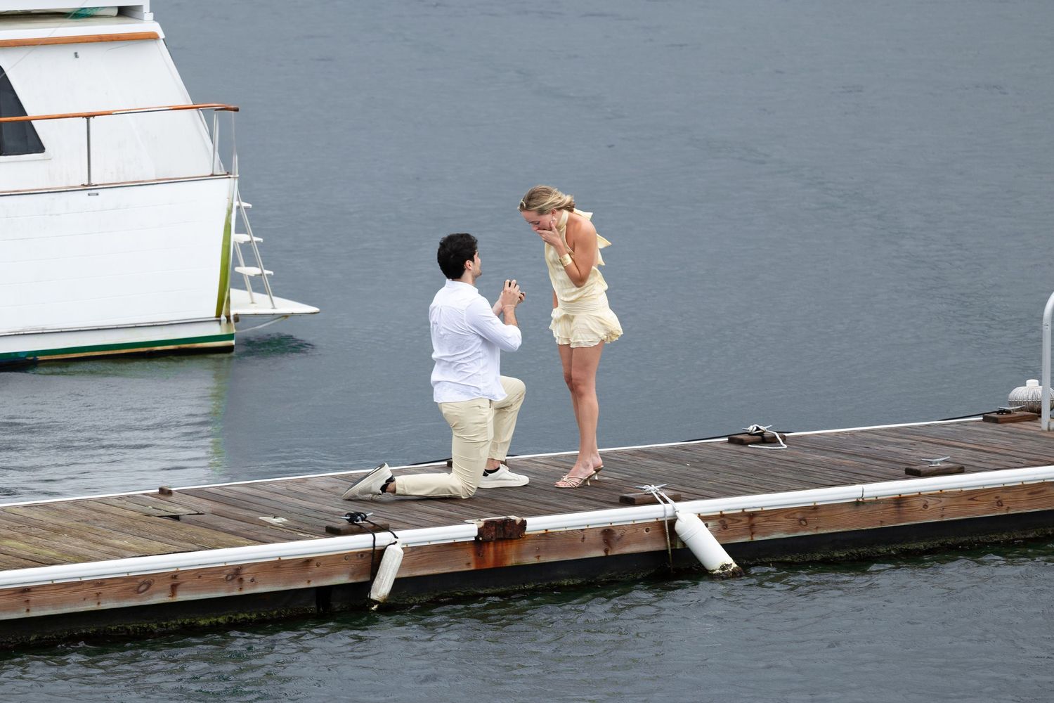 A proposal moment captured on a wooden dock with boats and water in the background.
