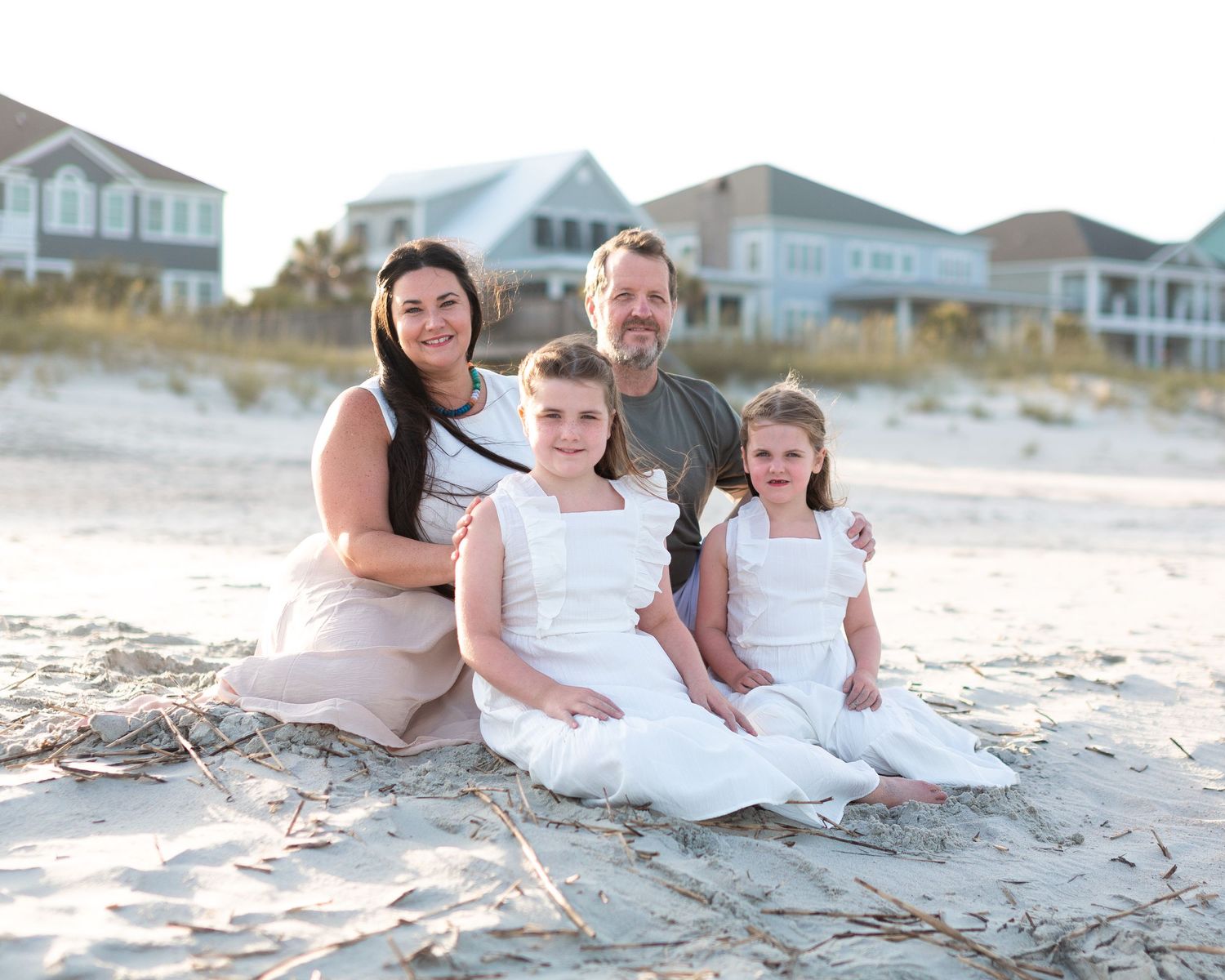 Group relaxes together on sandy beach with coastal homes visible in background.
