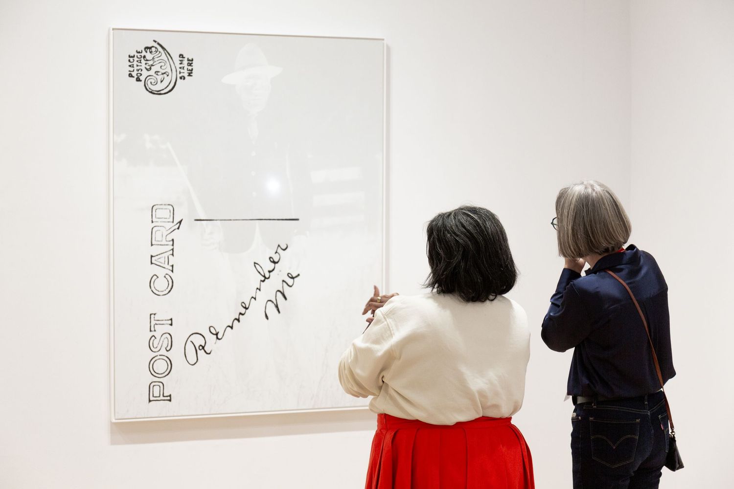 People viewing and discussing artwork displayed on a white gallery wall.