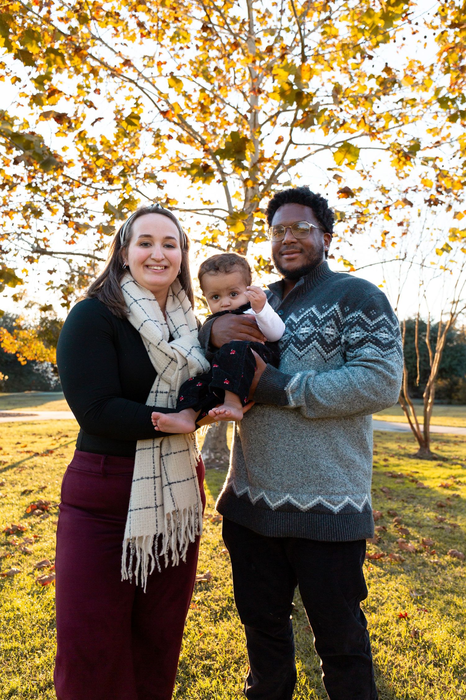 Family poses together outdoors during golden hour with autumn leaves and sunlight creating a warm atmosphere.