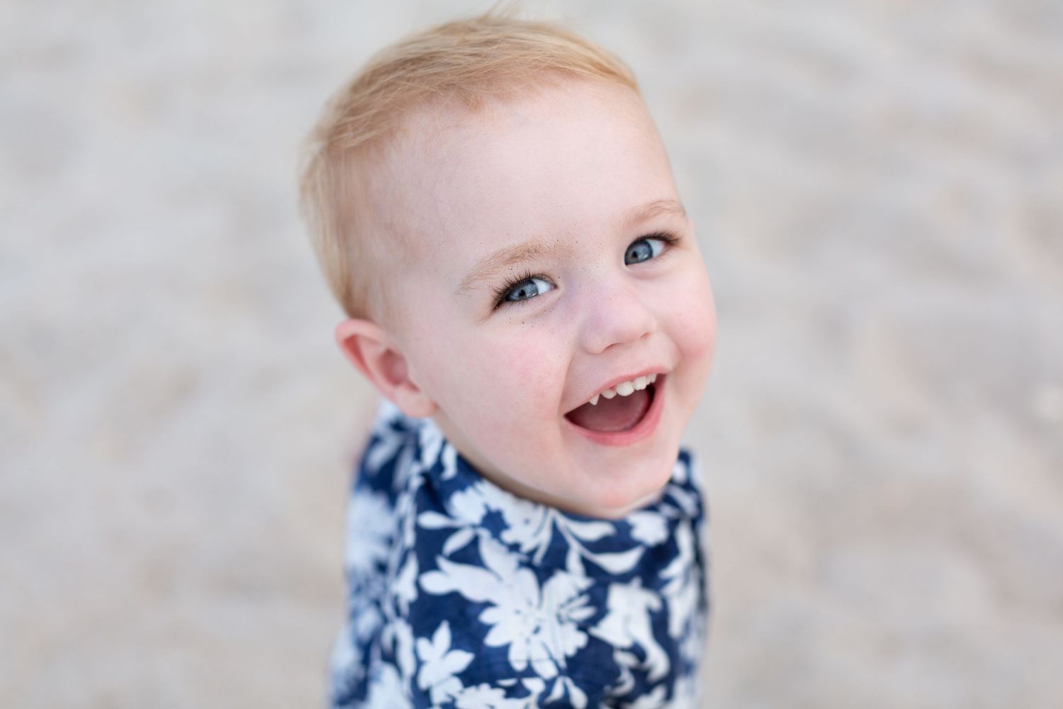 A baby wearing a blue and white floral dress smiles joyfully while sitting.