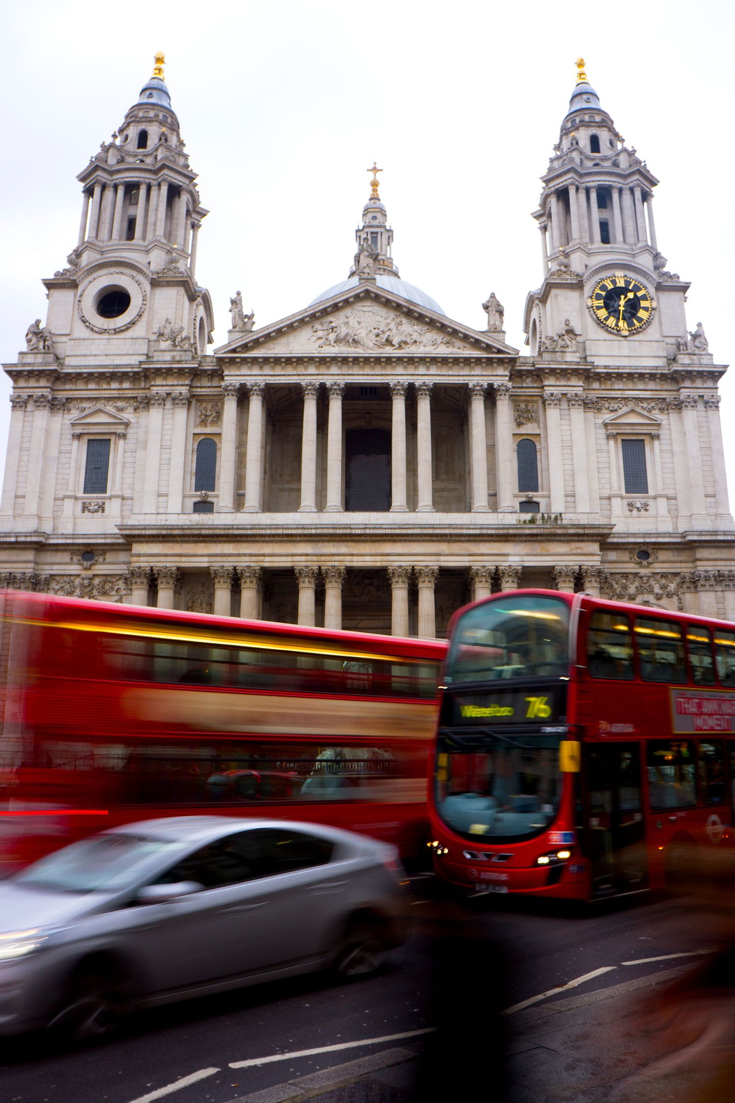 Red double-decker London bus speeding past St. Pauls Cathedral with motion blur on an overcast day.