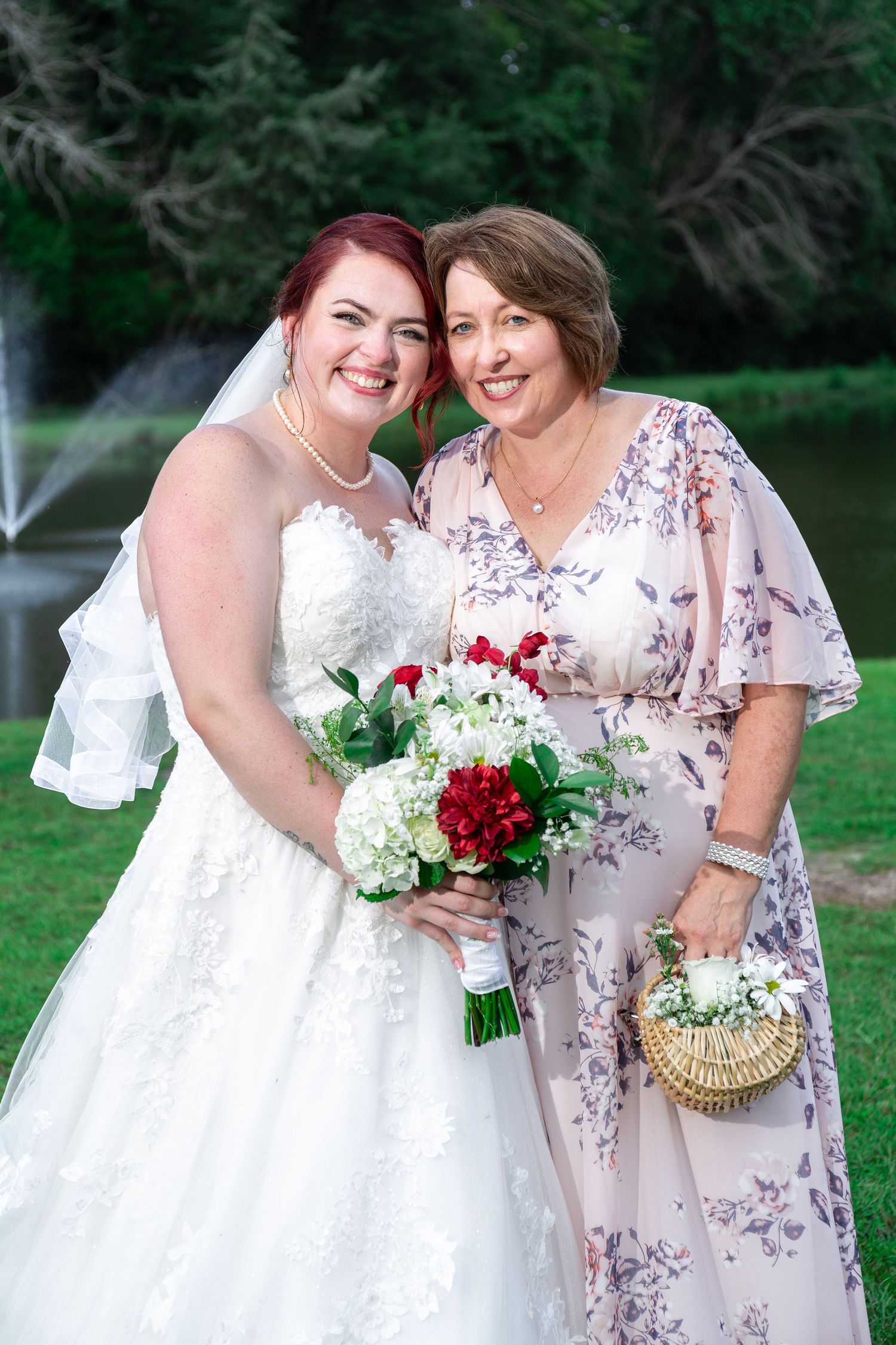 Wedding party members in white and floral dresses pose together outdoors holding bouquets.