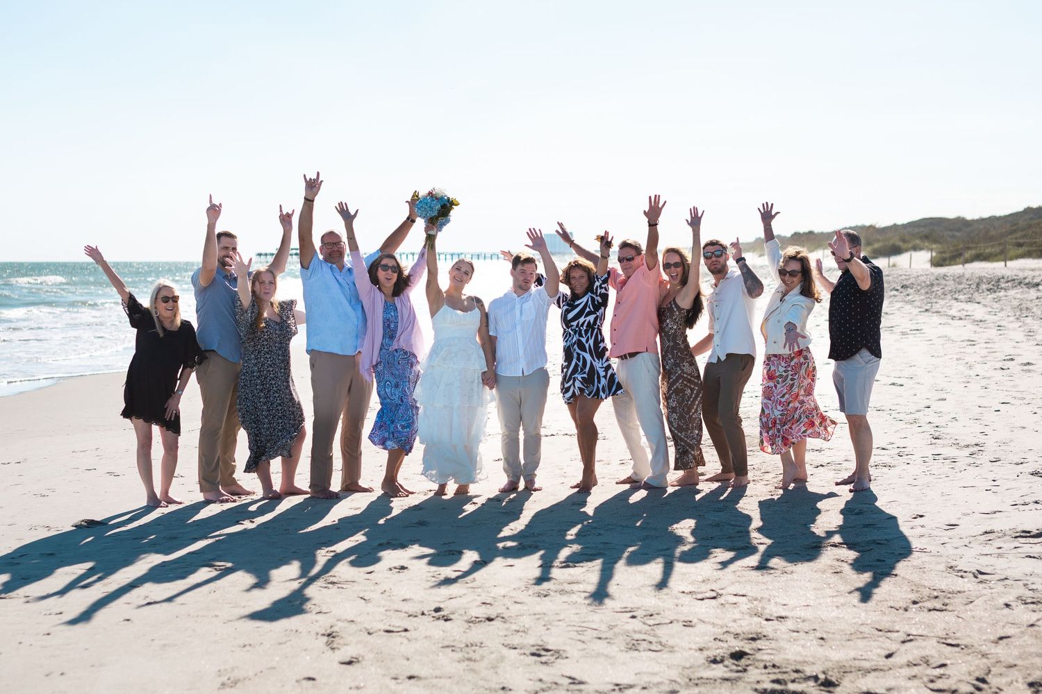 Group of people jumping and celebrating together on a sunny beach with ocean waves in the background.
