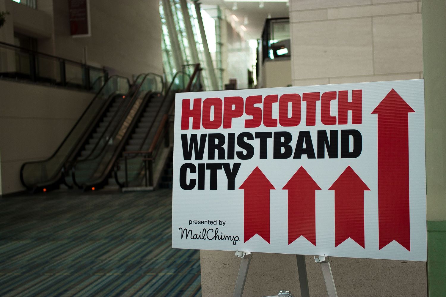 Red directional signs on white walls pointing to different areas including Hopscotch and Wristband.