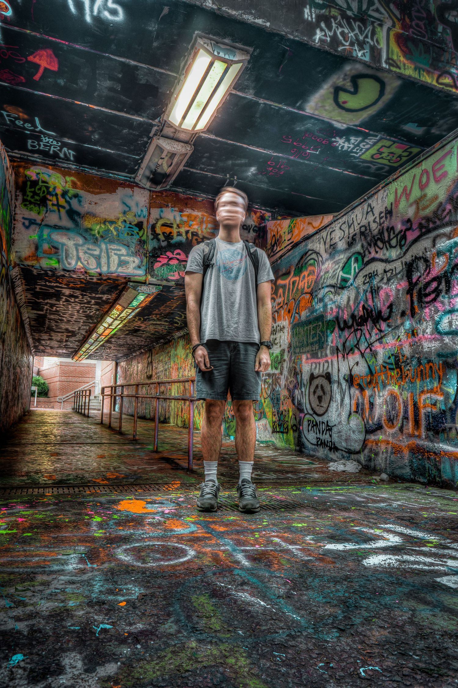 Young man standing in a graffiti-covered tunnel with colorful street art covering walls, ceiling, and floor.