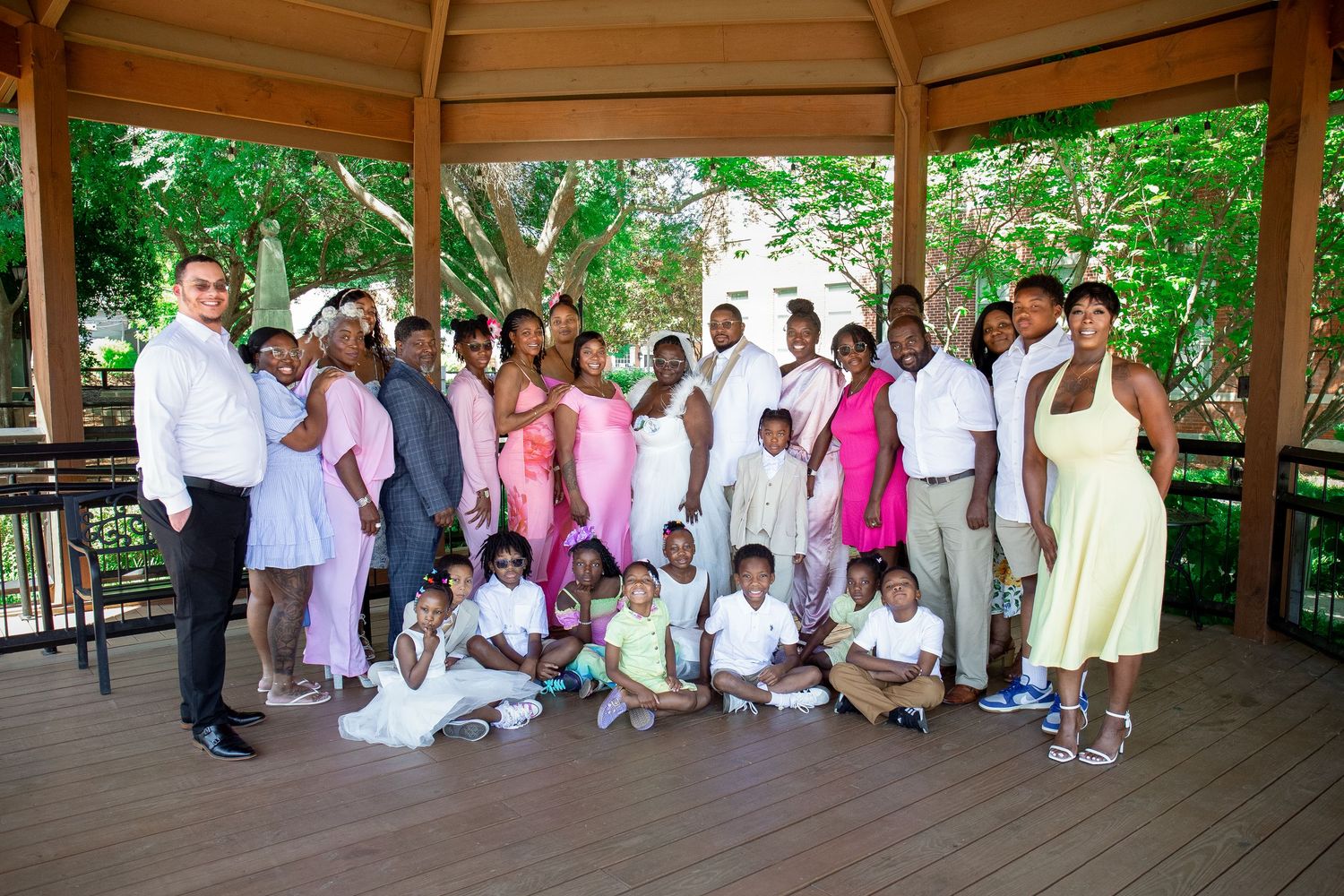 Large family group portrait posed under a gazebo outdoors, dressed in formal attire for a special occasion.