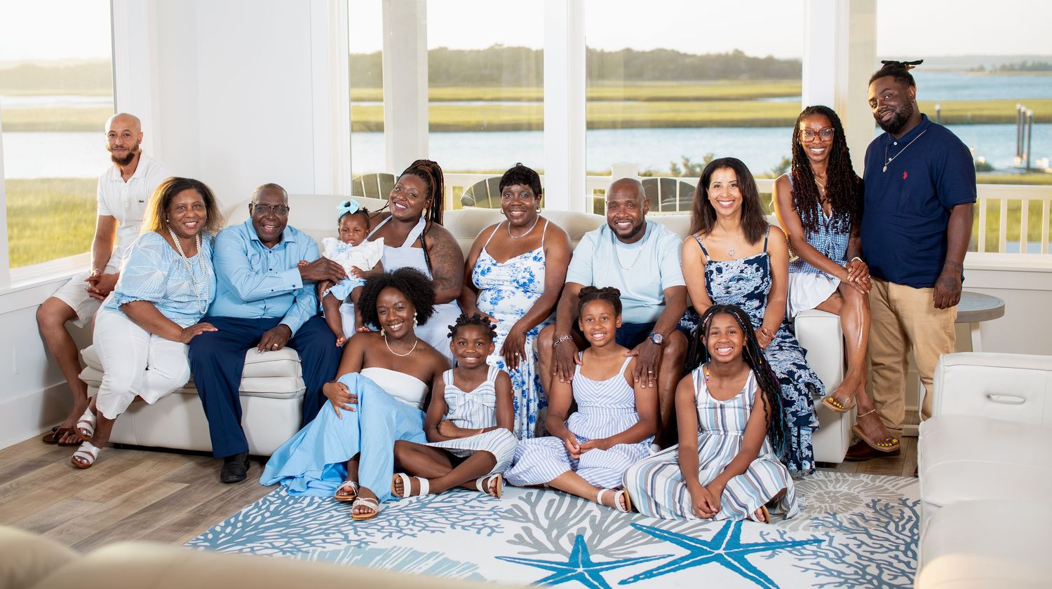 Family wearing coordinated blue and white outfits poses together on beach boardwalk during sunset photo session.
