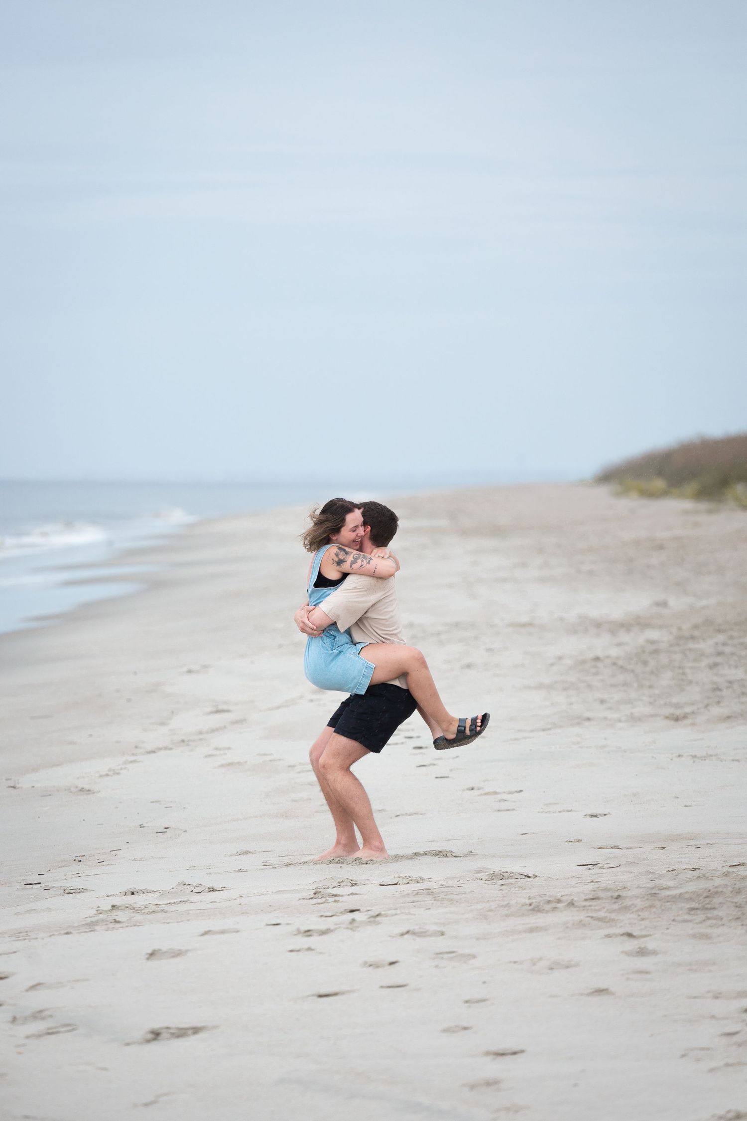 A couple embraces and shares a romantic moment together on a sandy beach during golden hour.
