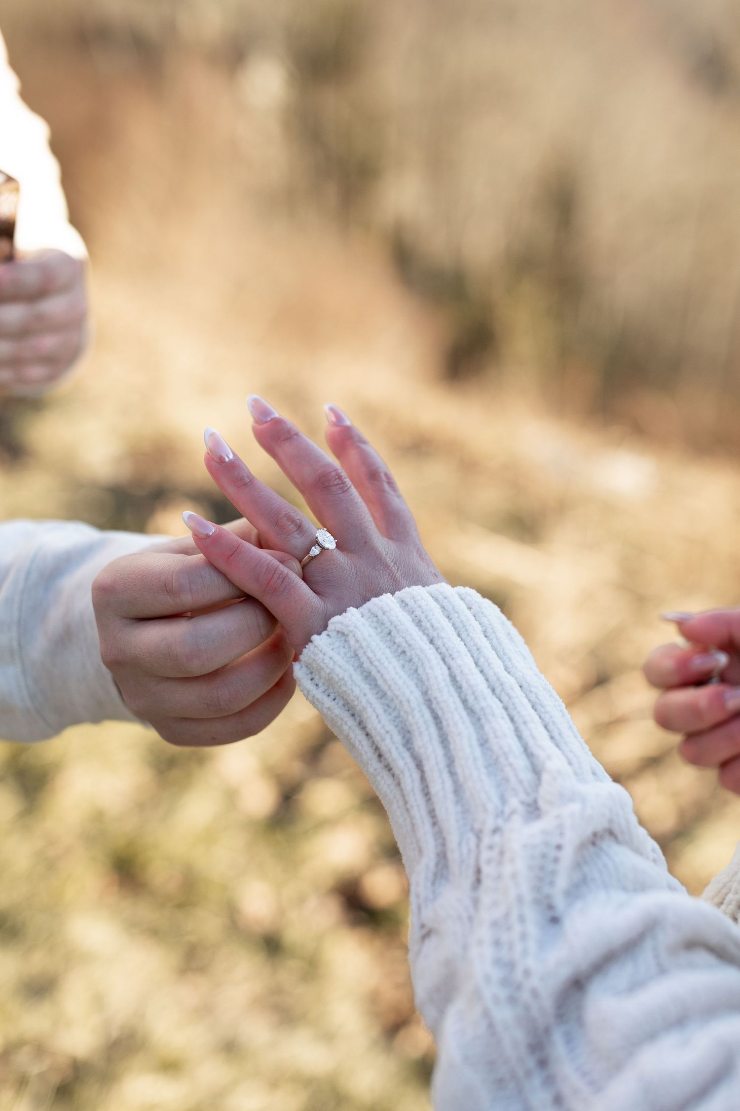 Close-up view of hands wearing a cozy white knit sweater sleeve against a soft blurred autumn background.