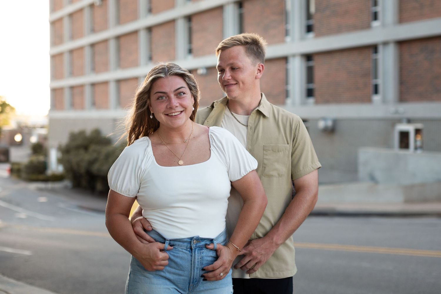 A couple embraces and laughs together while standing against a brick building exterior.