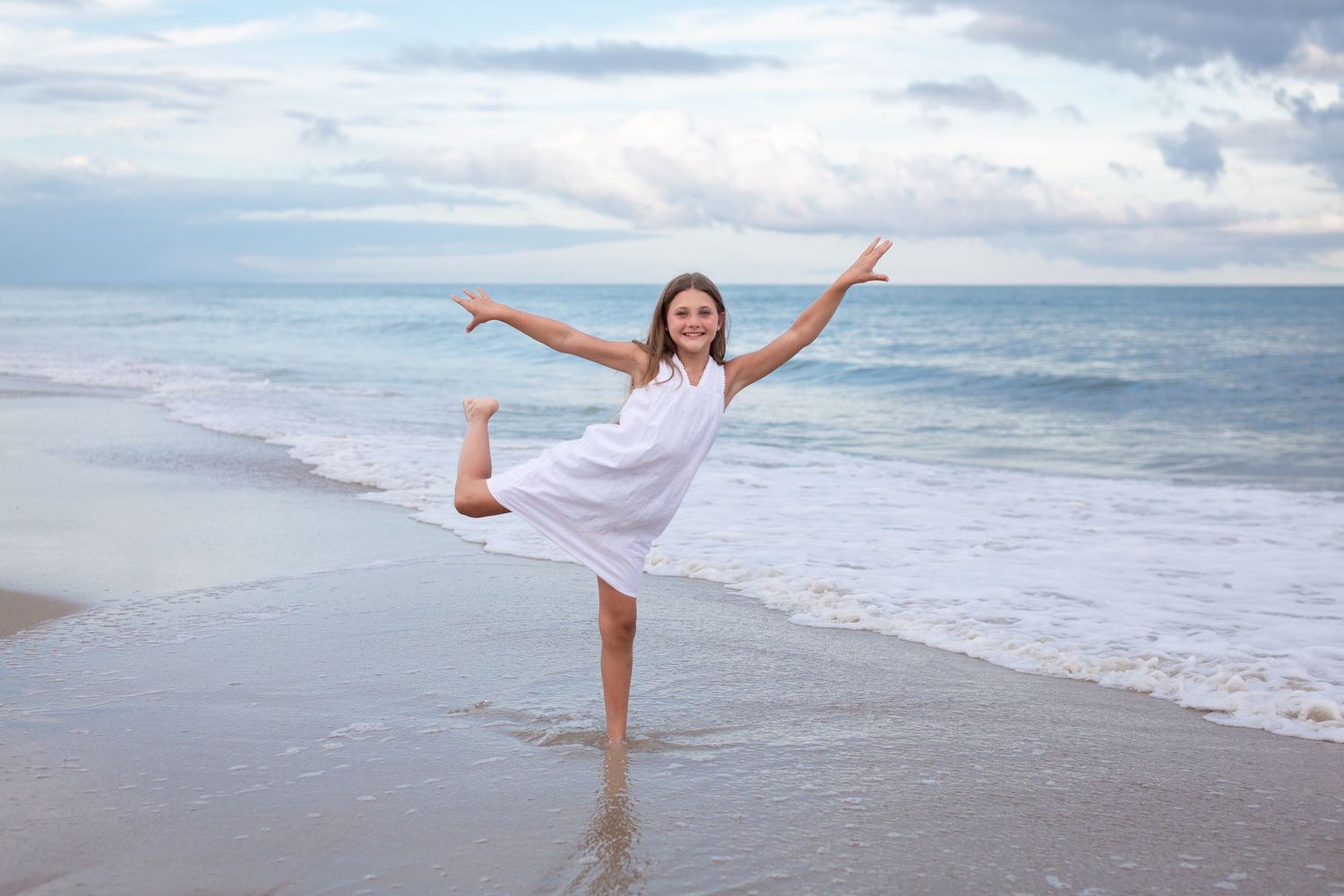 A joyful figure in a white dress dances on the beach with arms outstretched against an ocean backdrop.
