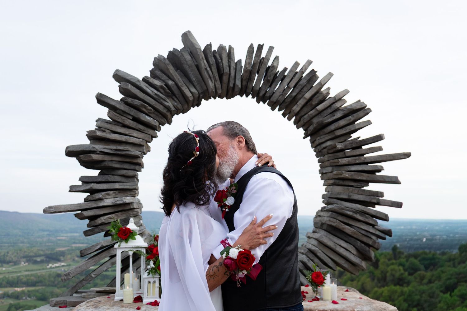 Couple sharing a kiss under a rustic wooden arch during an outdoor wedding ceremony with scenic views.