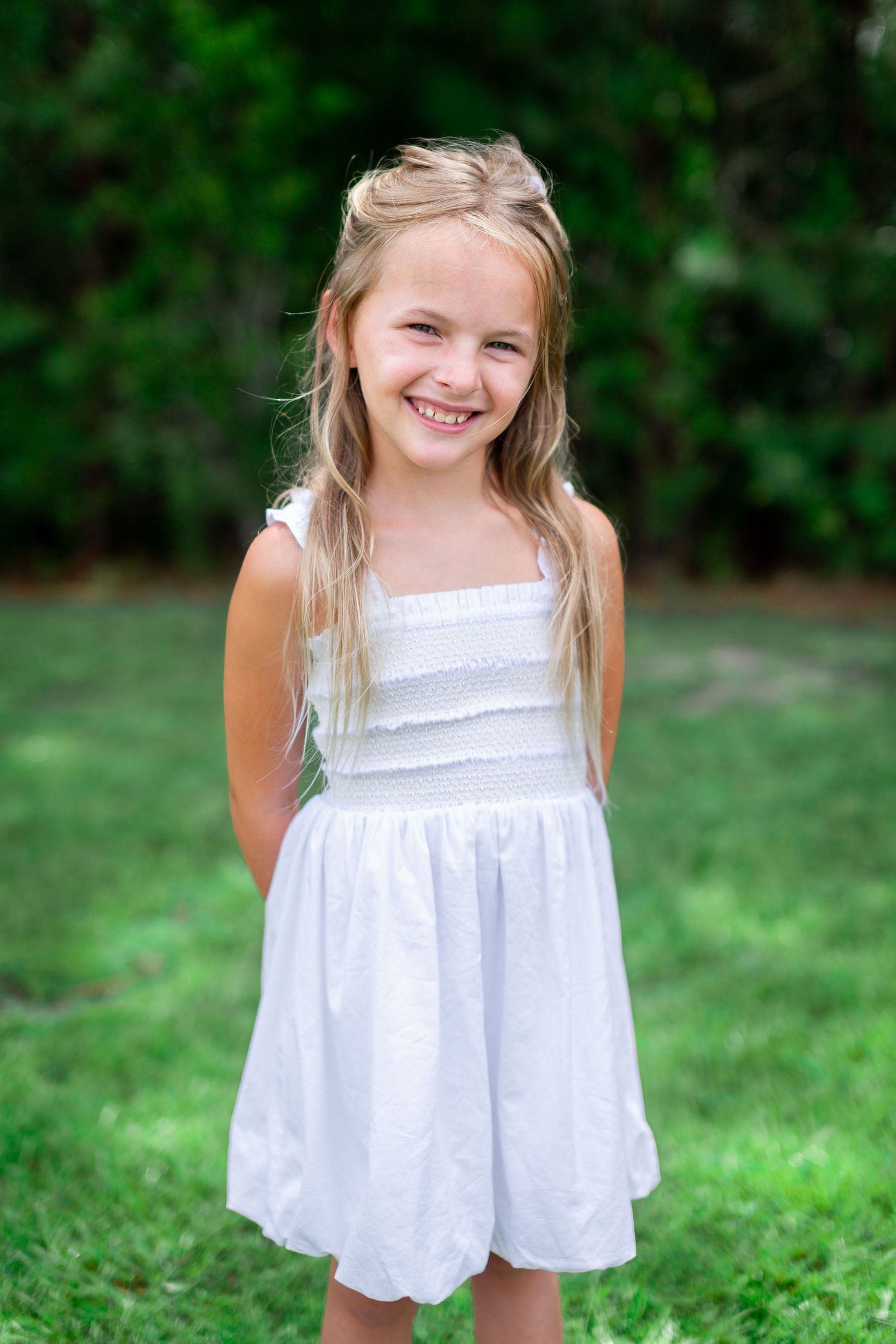Child wearing a white summer dress smiling outdoors on green grass.