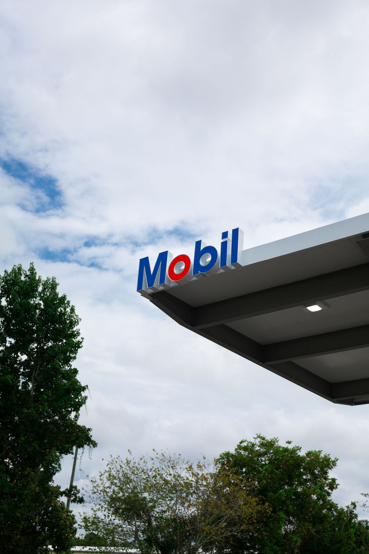 Mobil gas station sign against cloudy sky with trees visible in the background.