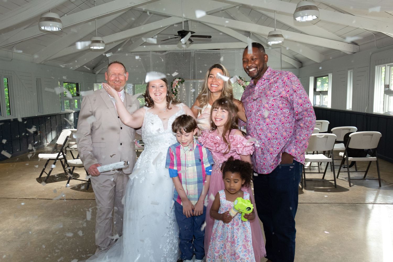 Wedding couple poses with family and friends in a decorated event hall, celebrating their special day.