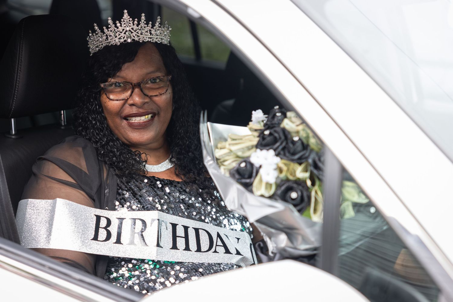 Drive-by birthday celebration with people in cars waving and holding celebratory signs.