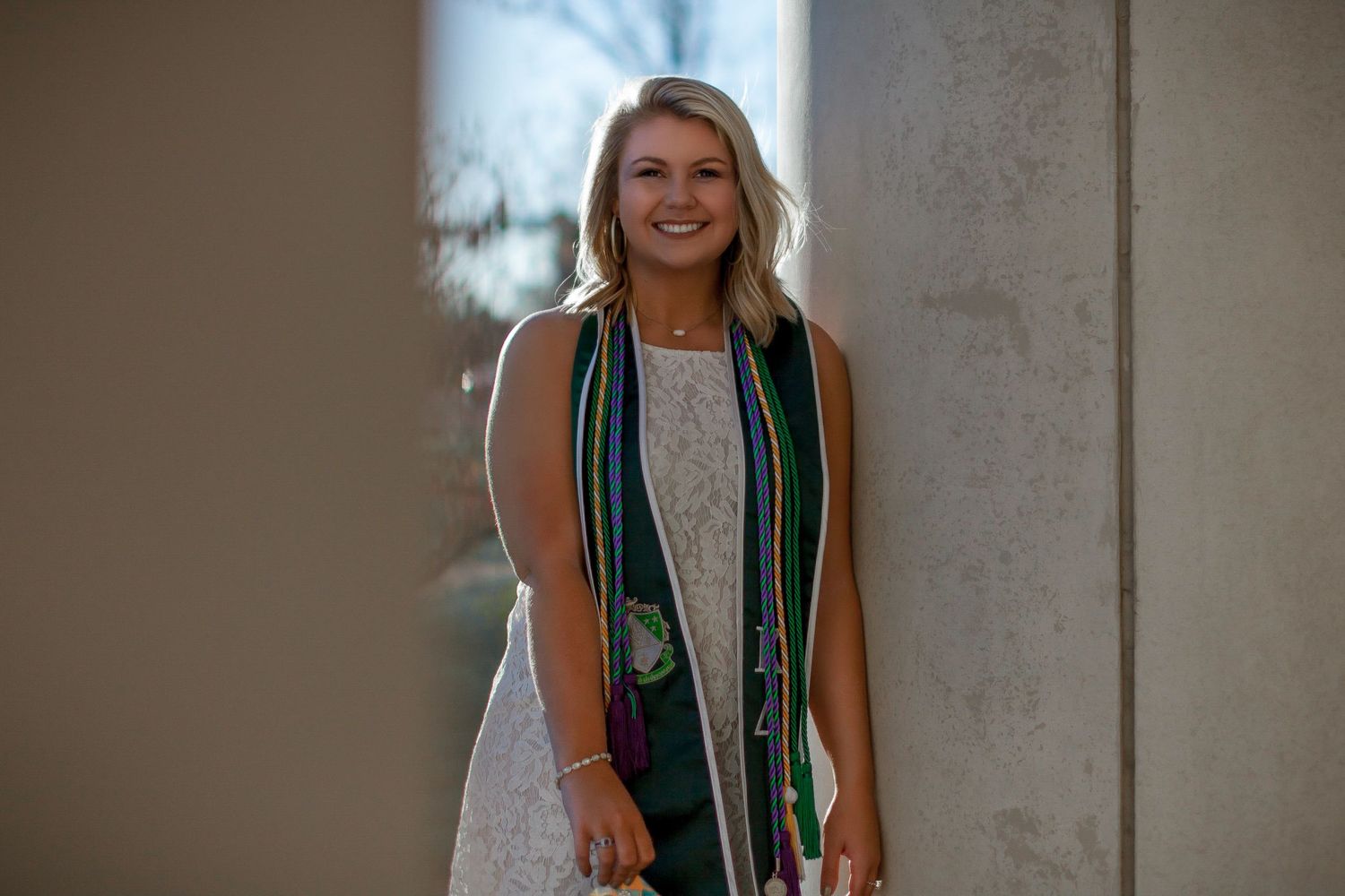 Graduate in green and white graduation stole poses against concrete wall in multiple candid shots.