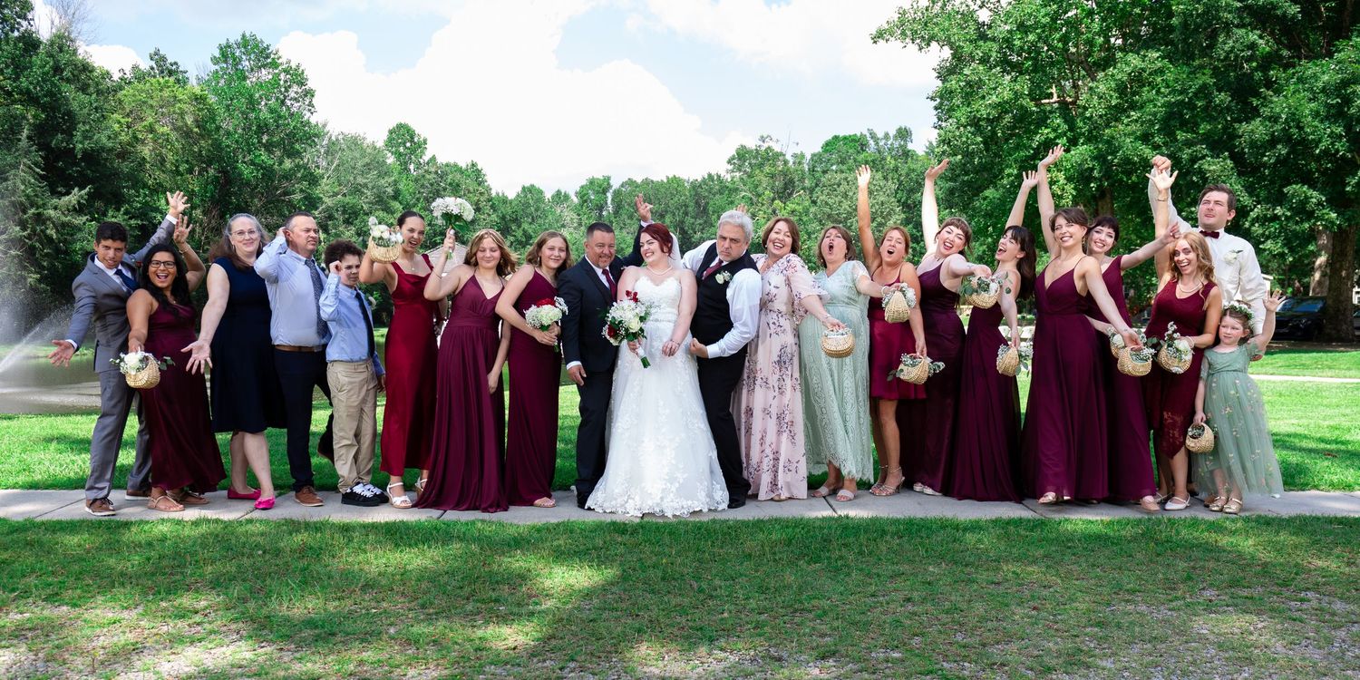 Wedding party in burgundy dresses and suits poses outdoors on a sunny day.