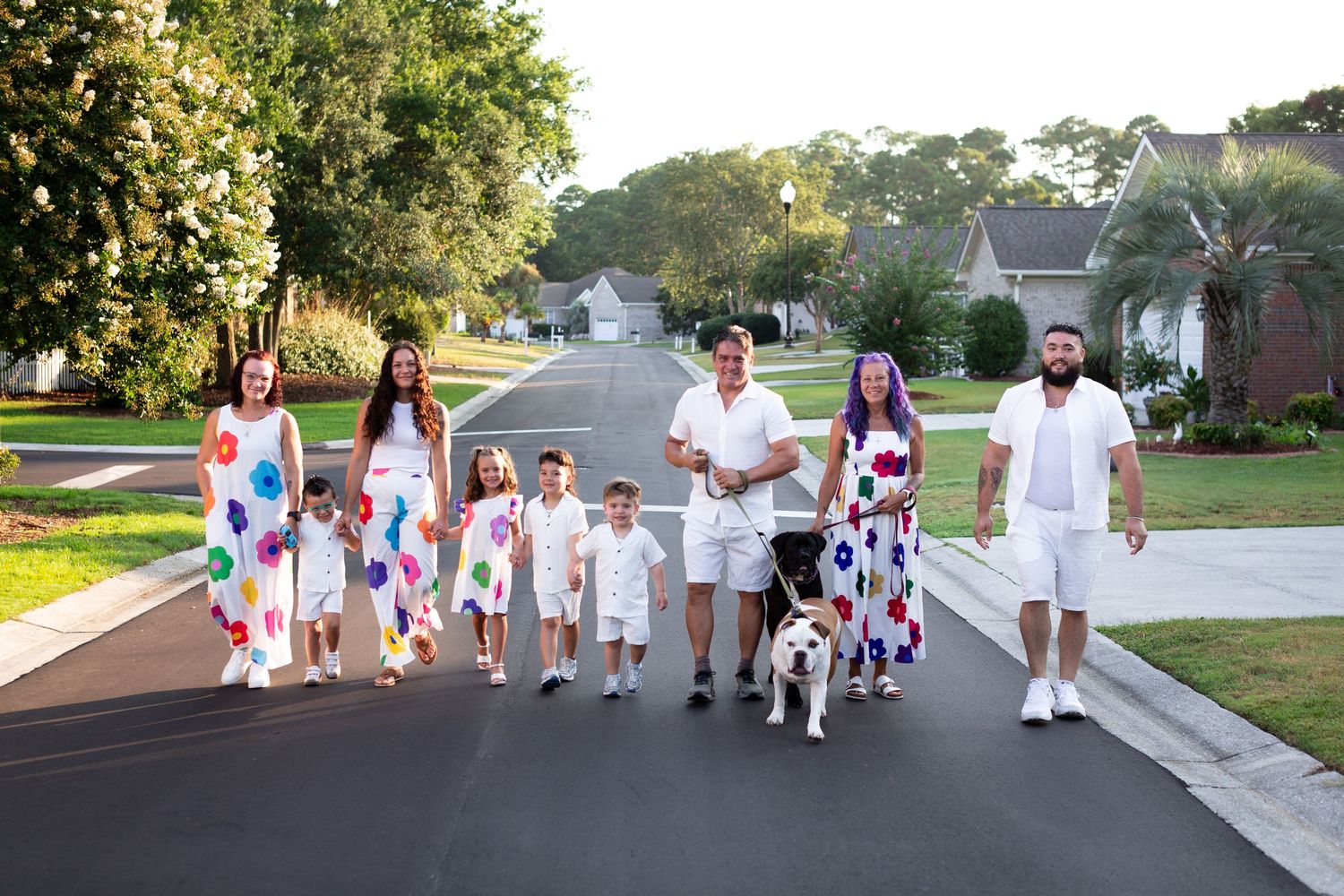 Family walking together on suburban street at sunset wearing coordinated white and floral outfits.