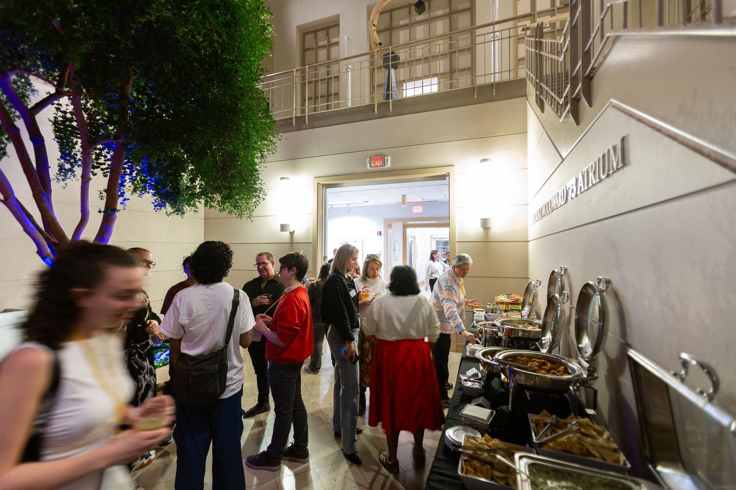 Crowded indoor hallway with people walking past decorative elements and artwork.
