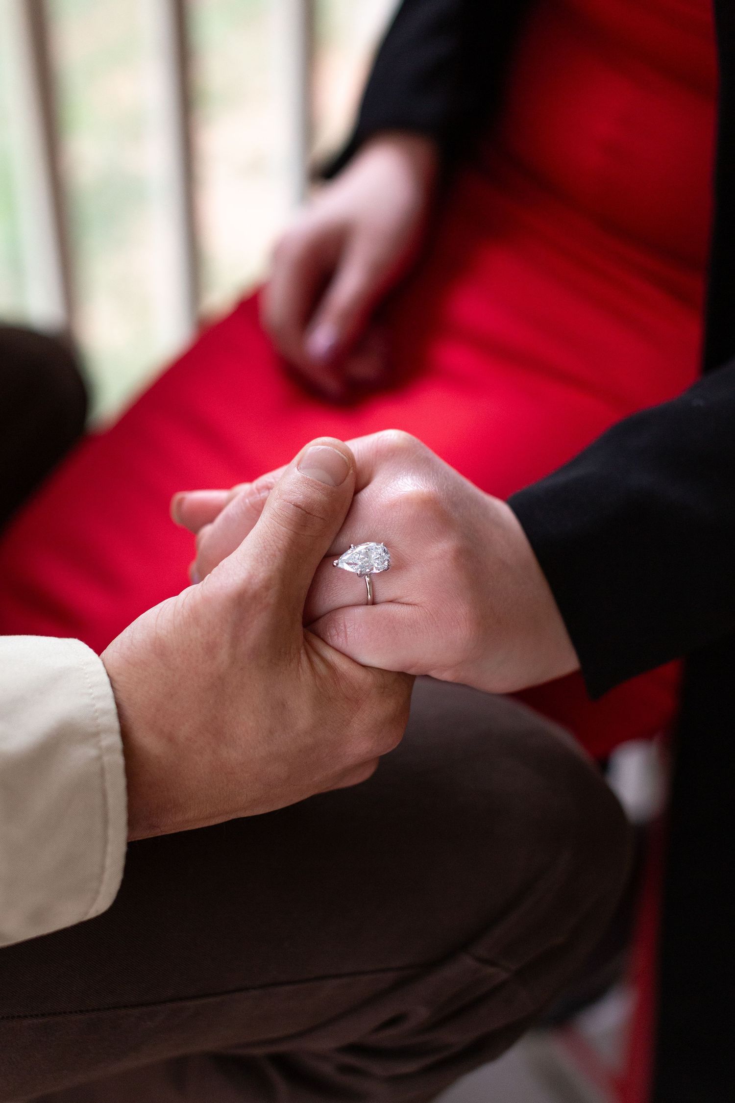 Close-up sequence of hands exchanging an engagement ring with a sparkling diamond on a red background.
