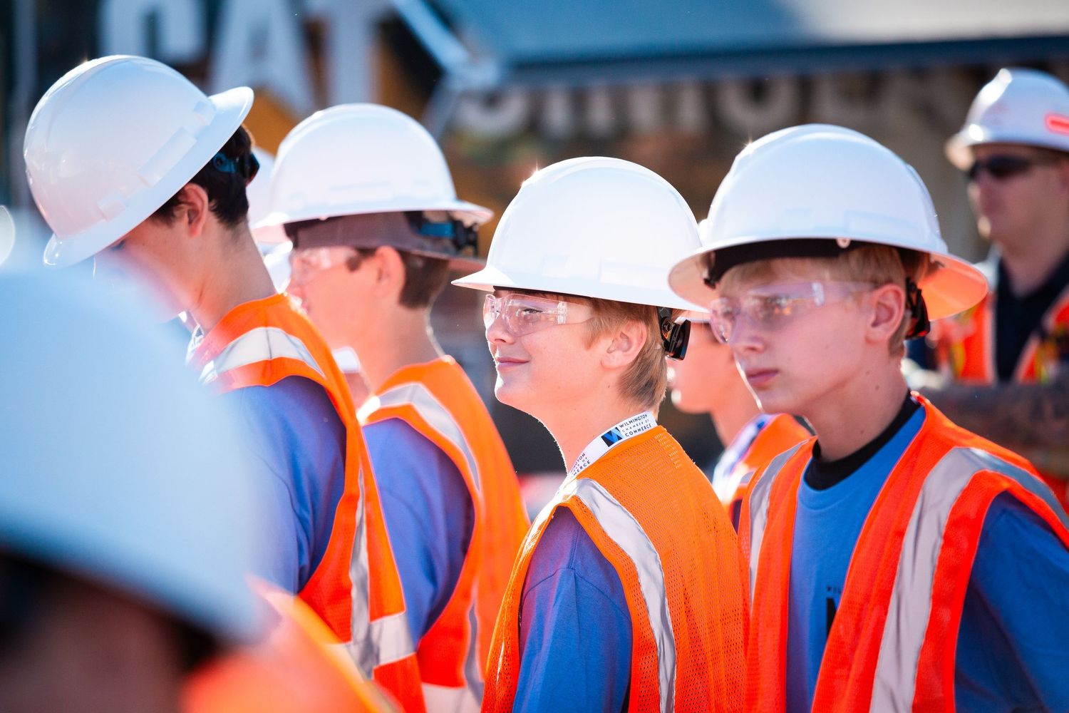 Construction workers in orange safety vests and white hard hats stand together at a job site.