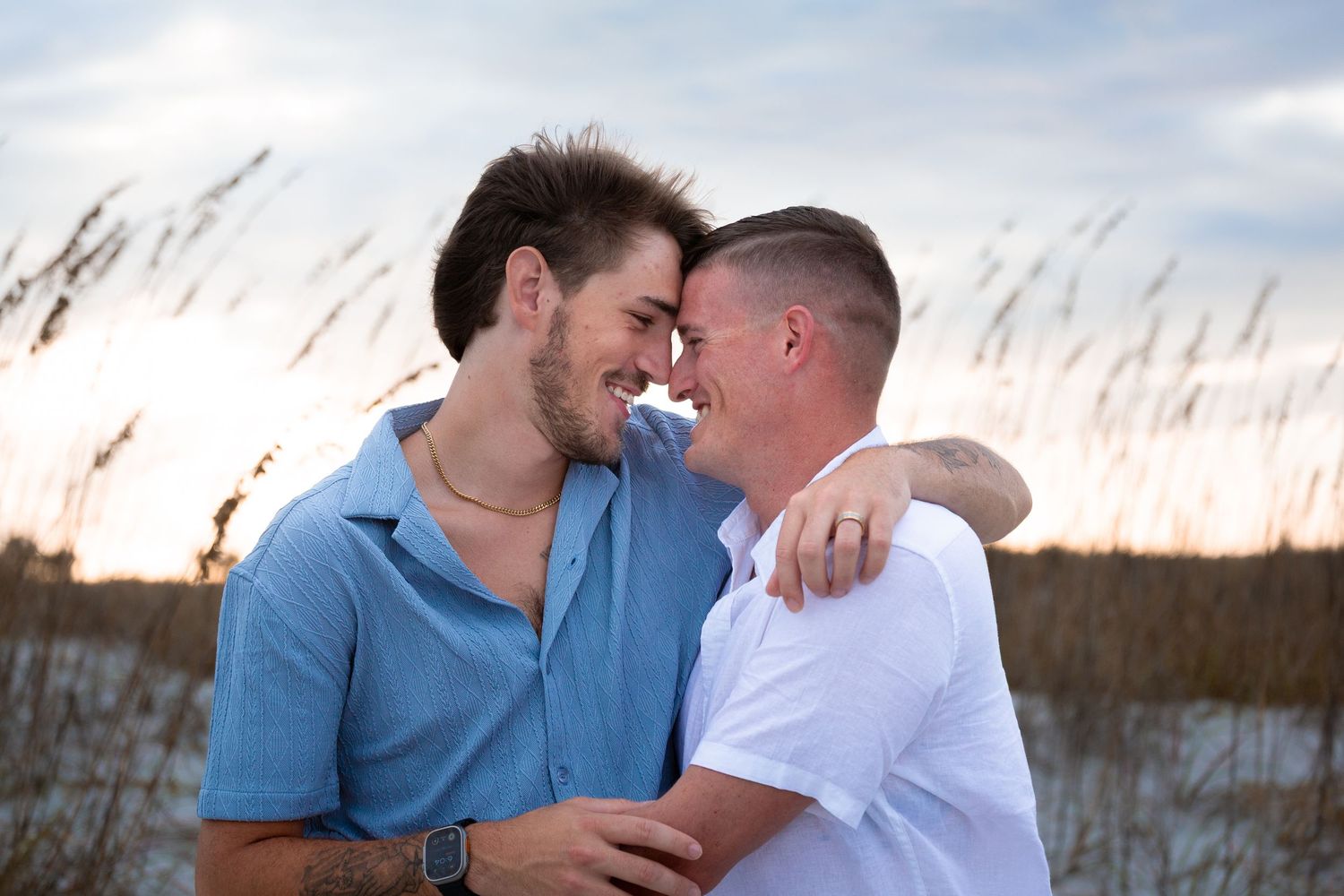 A couple shares an intimate moment among beach grass at sunset.