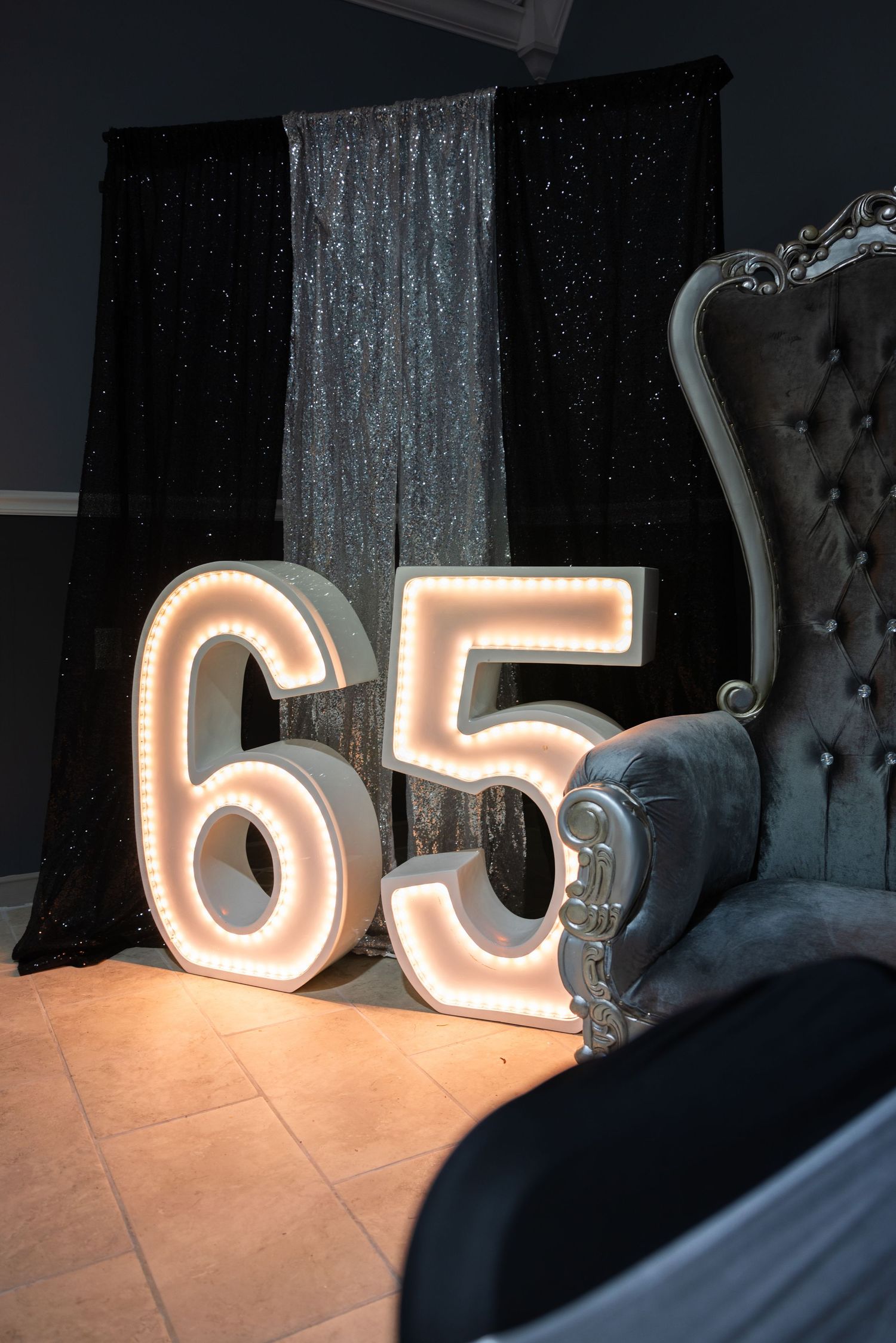Large illuminated numbers '65' displayed against a dark backdrop with silver curtains.