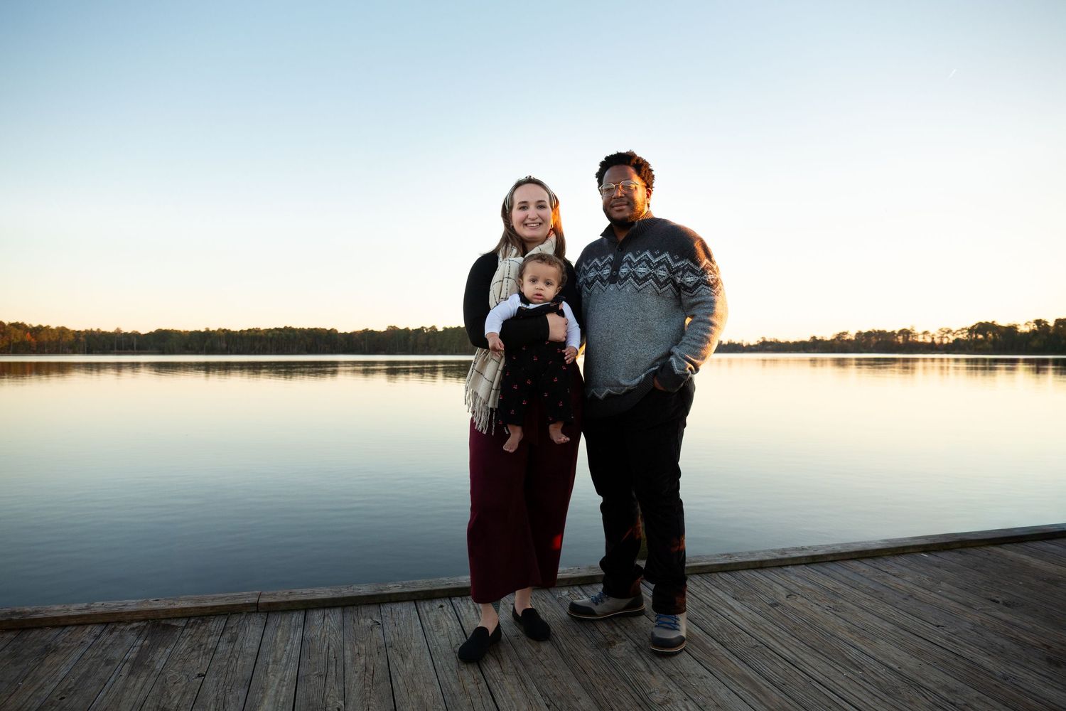 Group gathered on a lakeside dock during golden hour with calm water and trees in background.