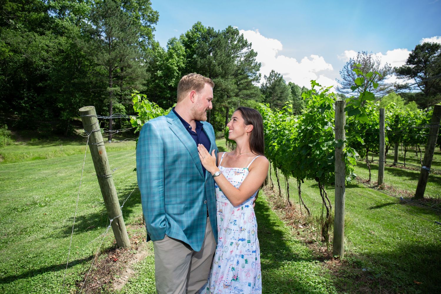 Couple sharing a romantic moment in a lush vineyard, man in blue blazer and woman in floral dress.