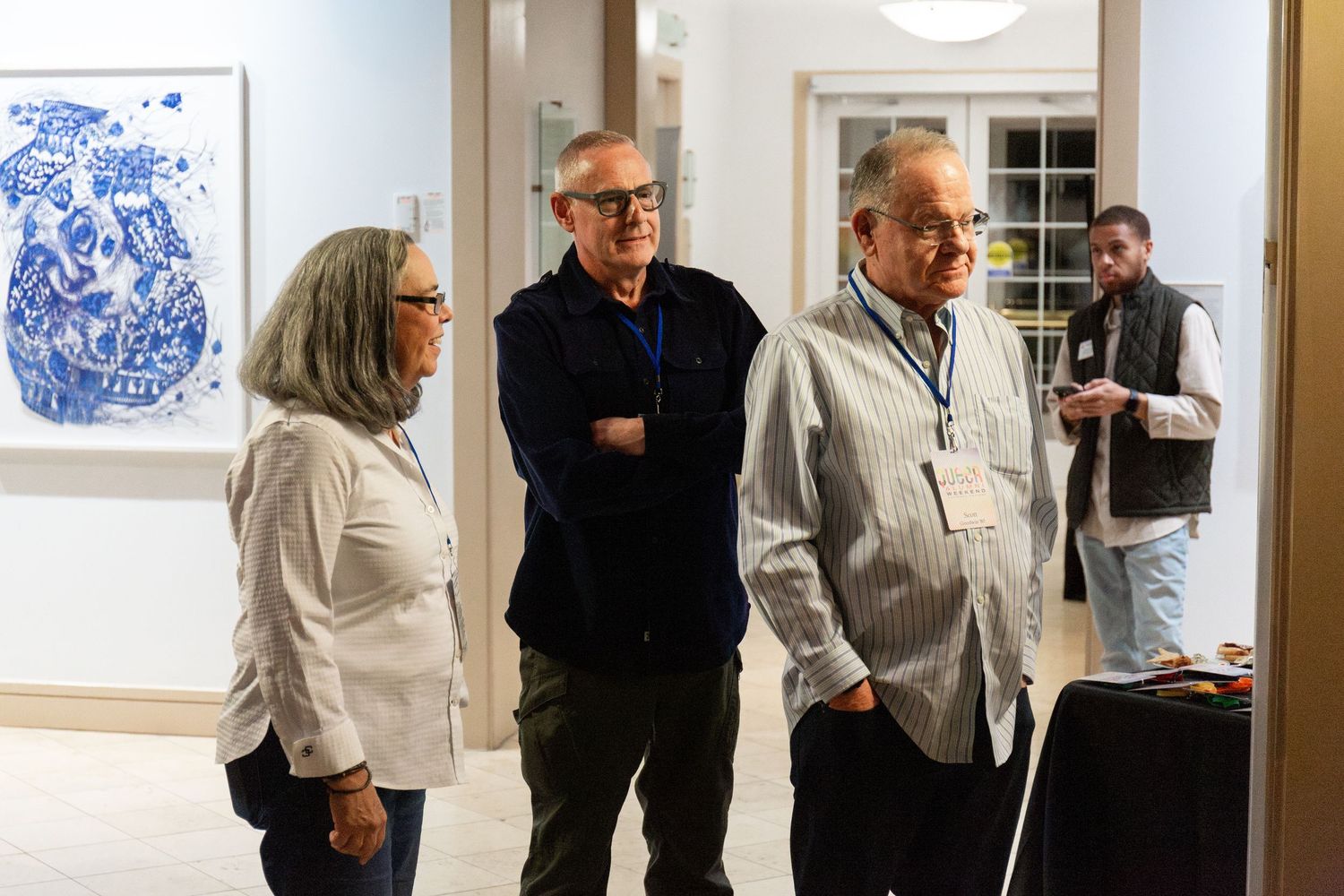 Art gallery visitors examine blue and white artwork displayed on white walls.