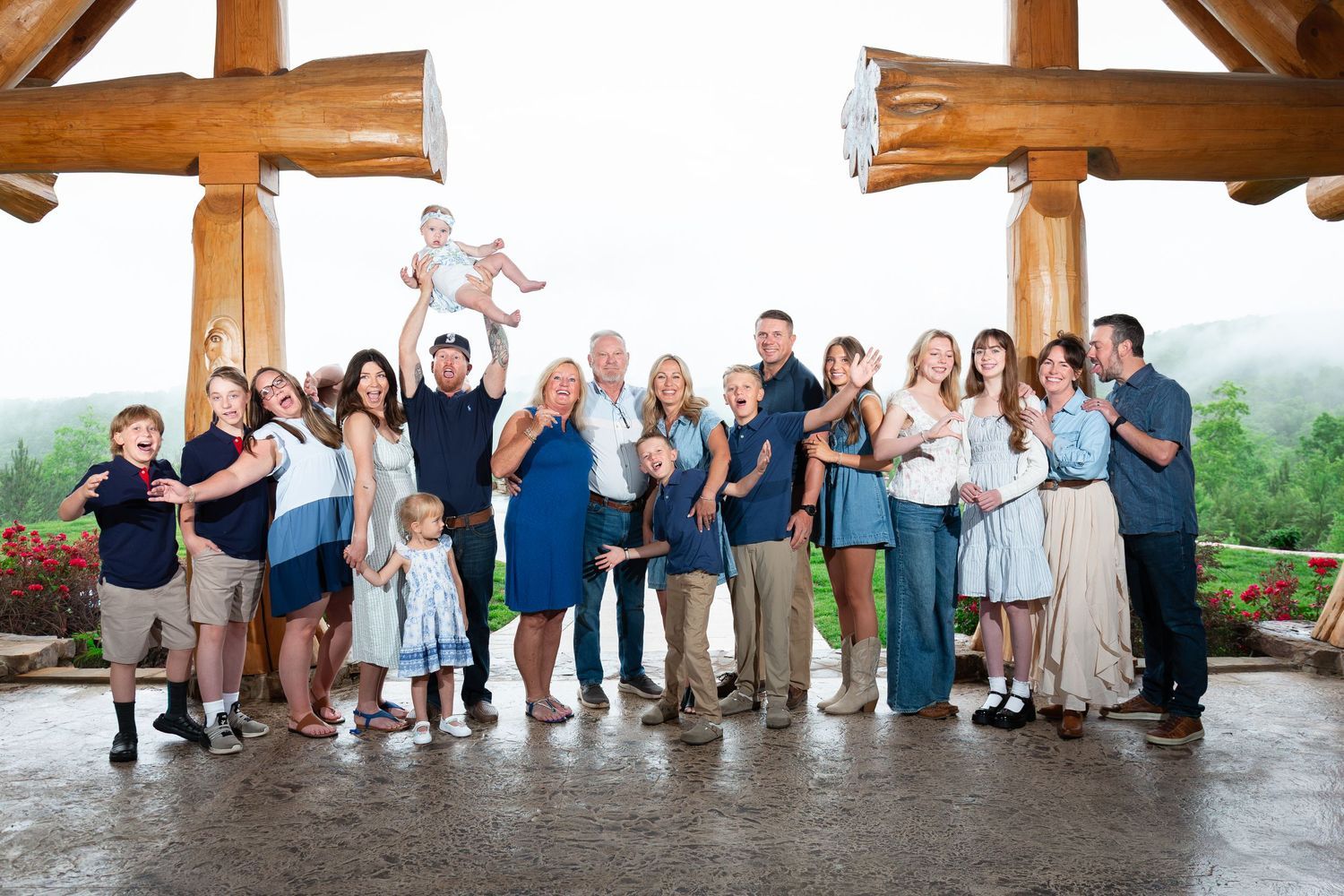 Large multigenerational family poses together under a rustic timber pavilion with misty green mountains behind them.