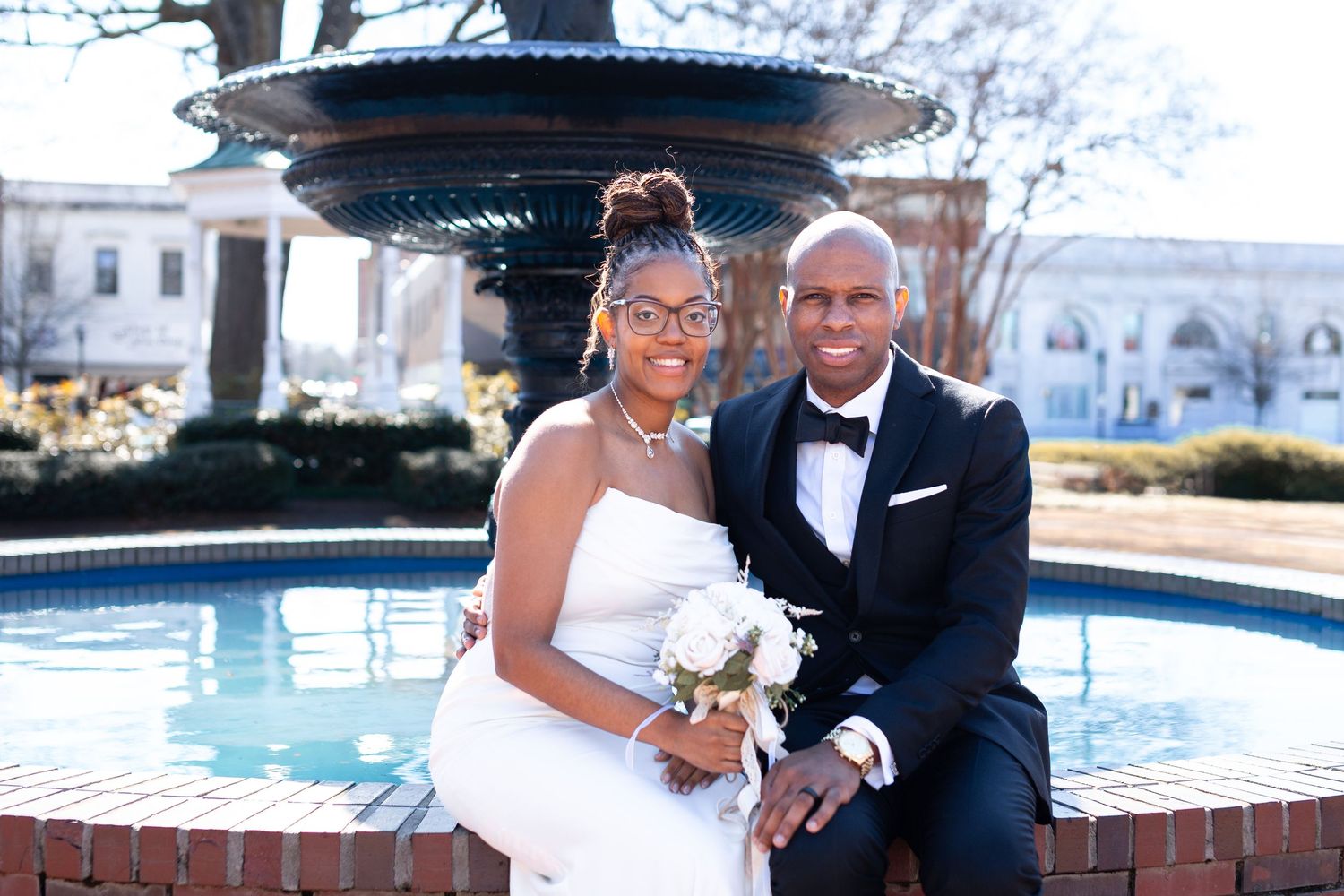 Elegant couple poses together in formal wedding attire near a fountain on their special day.