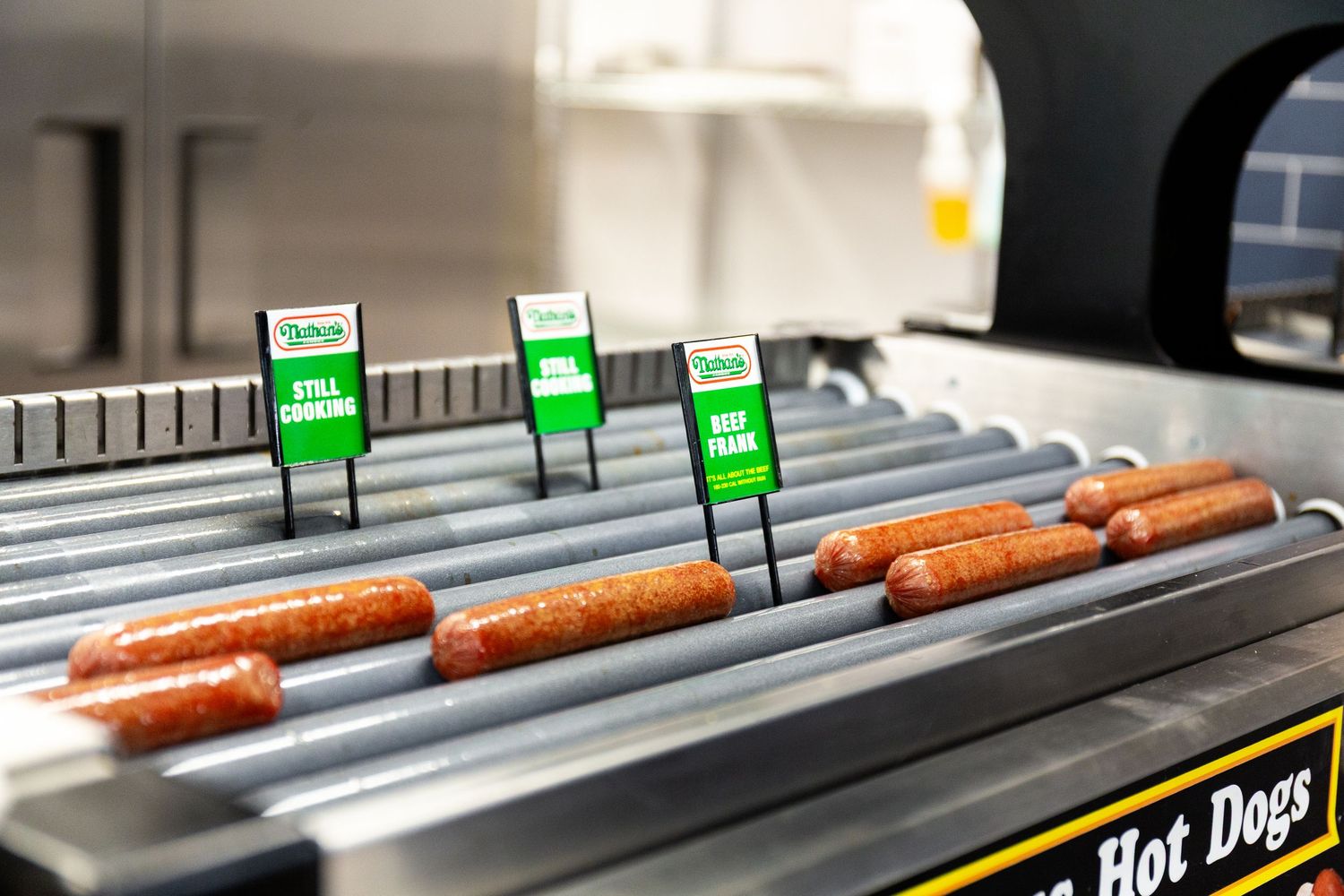 Hot dogs rotate on stainless steel rollers at a concession stand or convenience store display.