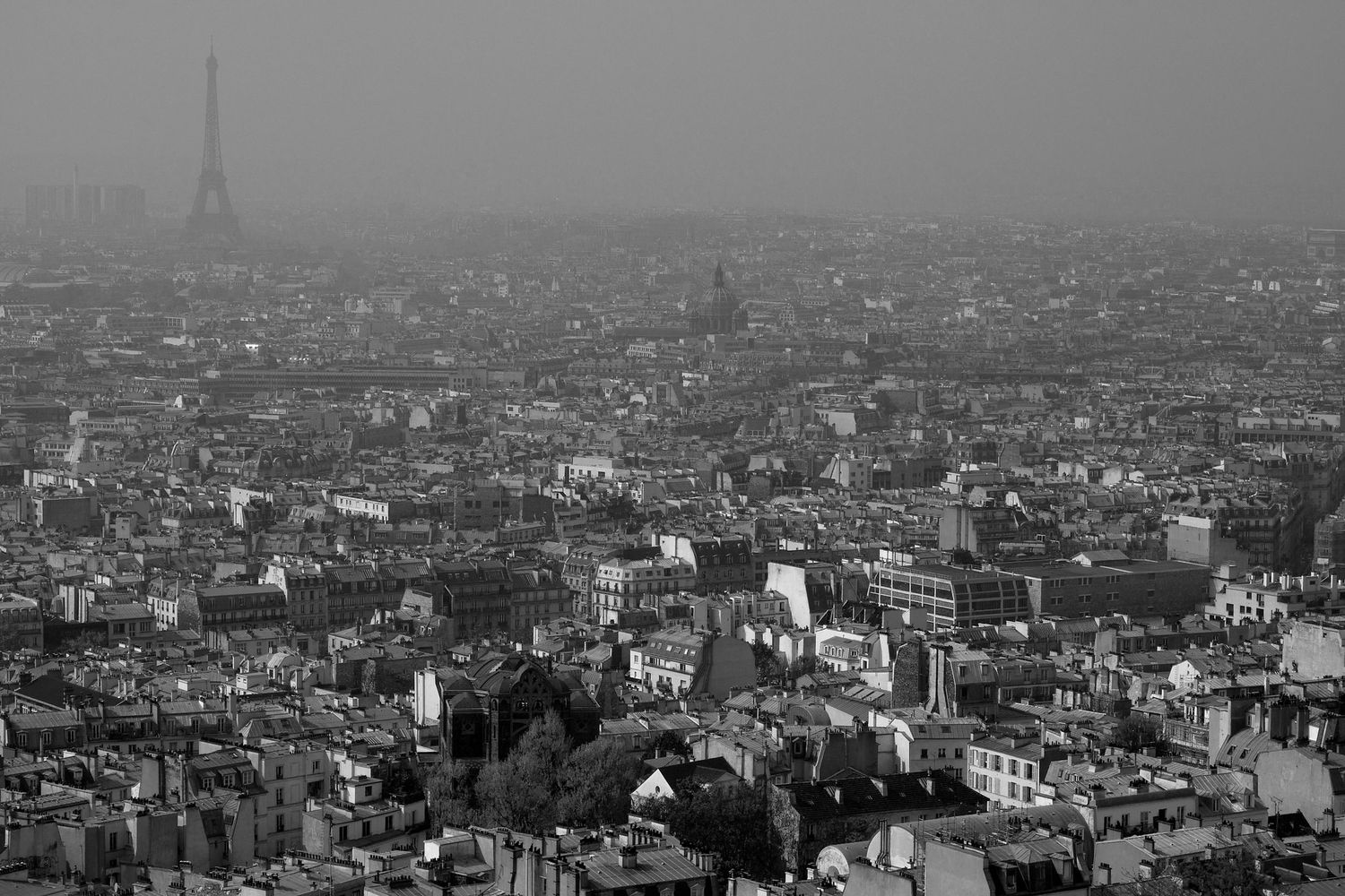 Black and white aerial view of Paris cityscape with Eiffel Tower in misty background.