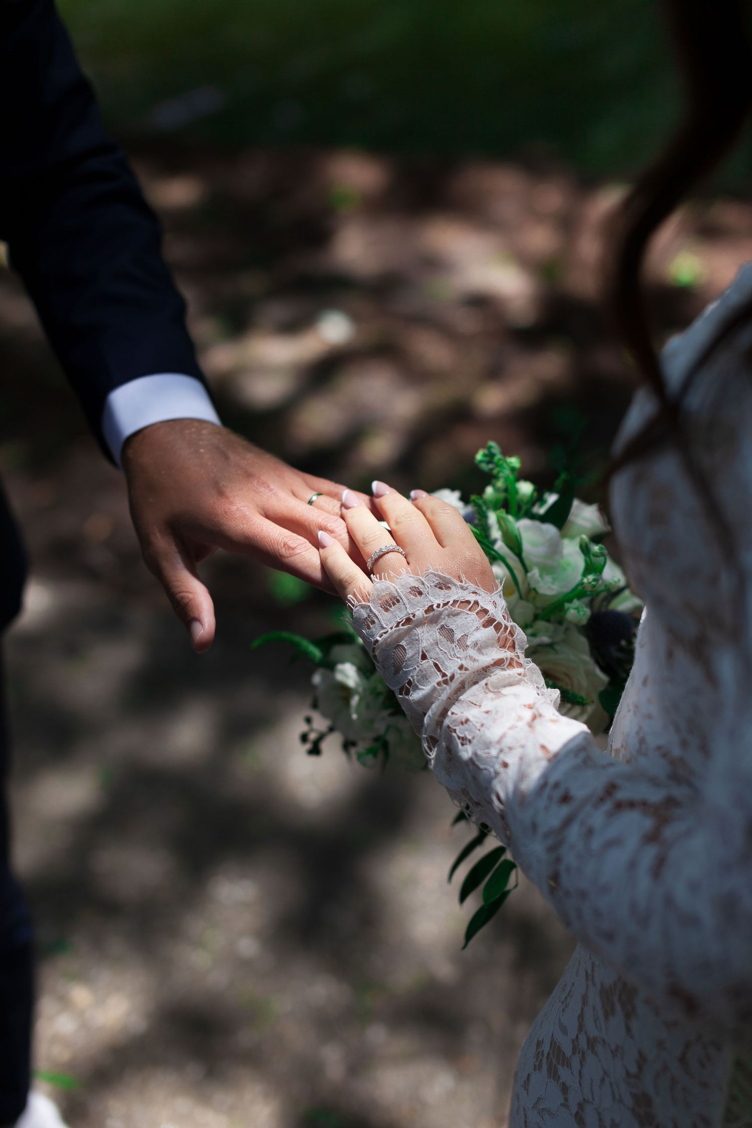 Close-up view of hands wearing delicate white lace against a dark natural background.