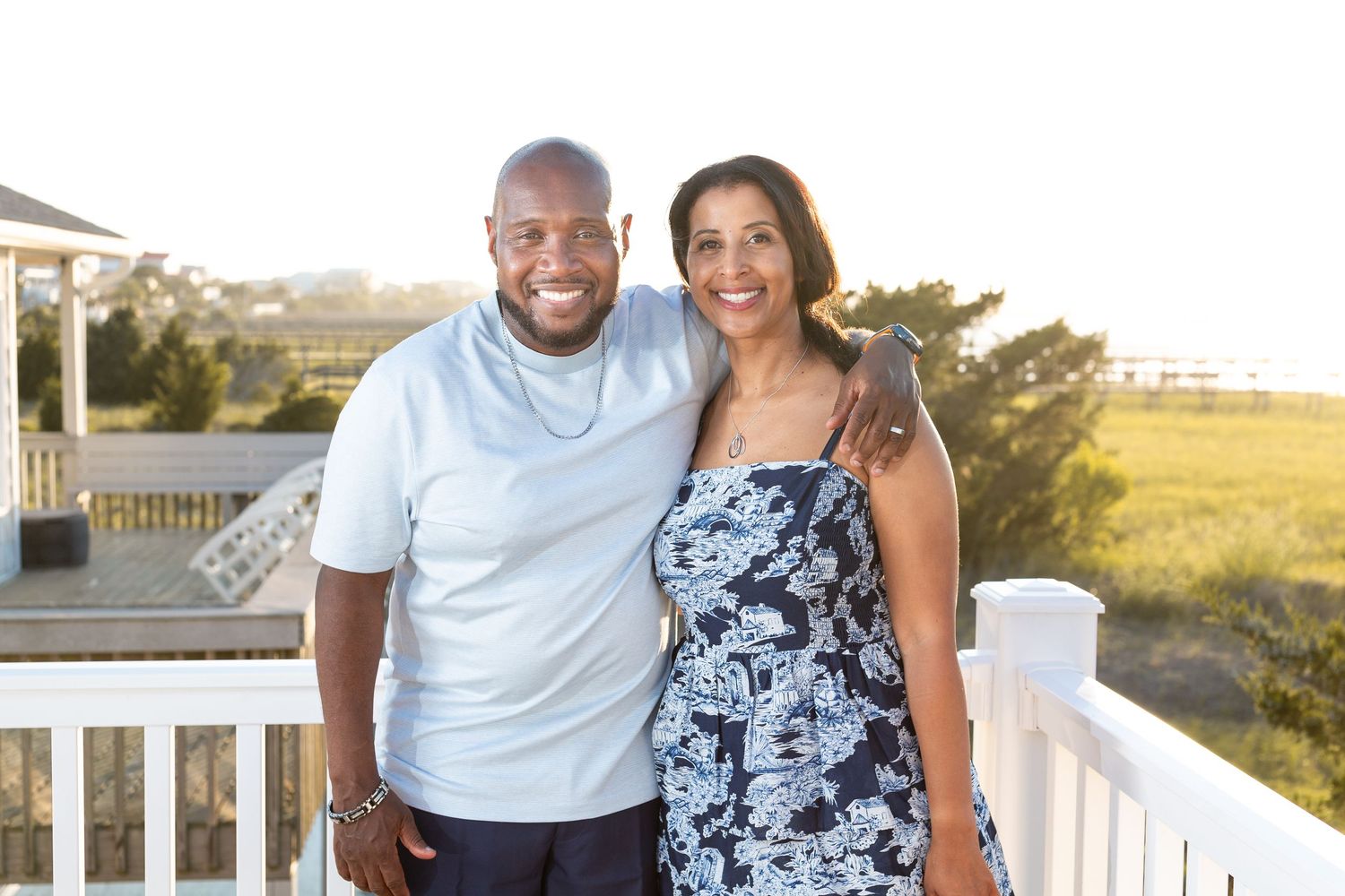 Happy couple embracing on a deck during golden hour with scenic background.