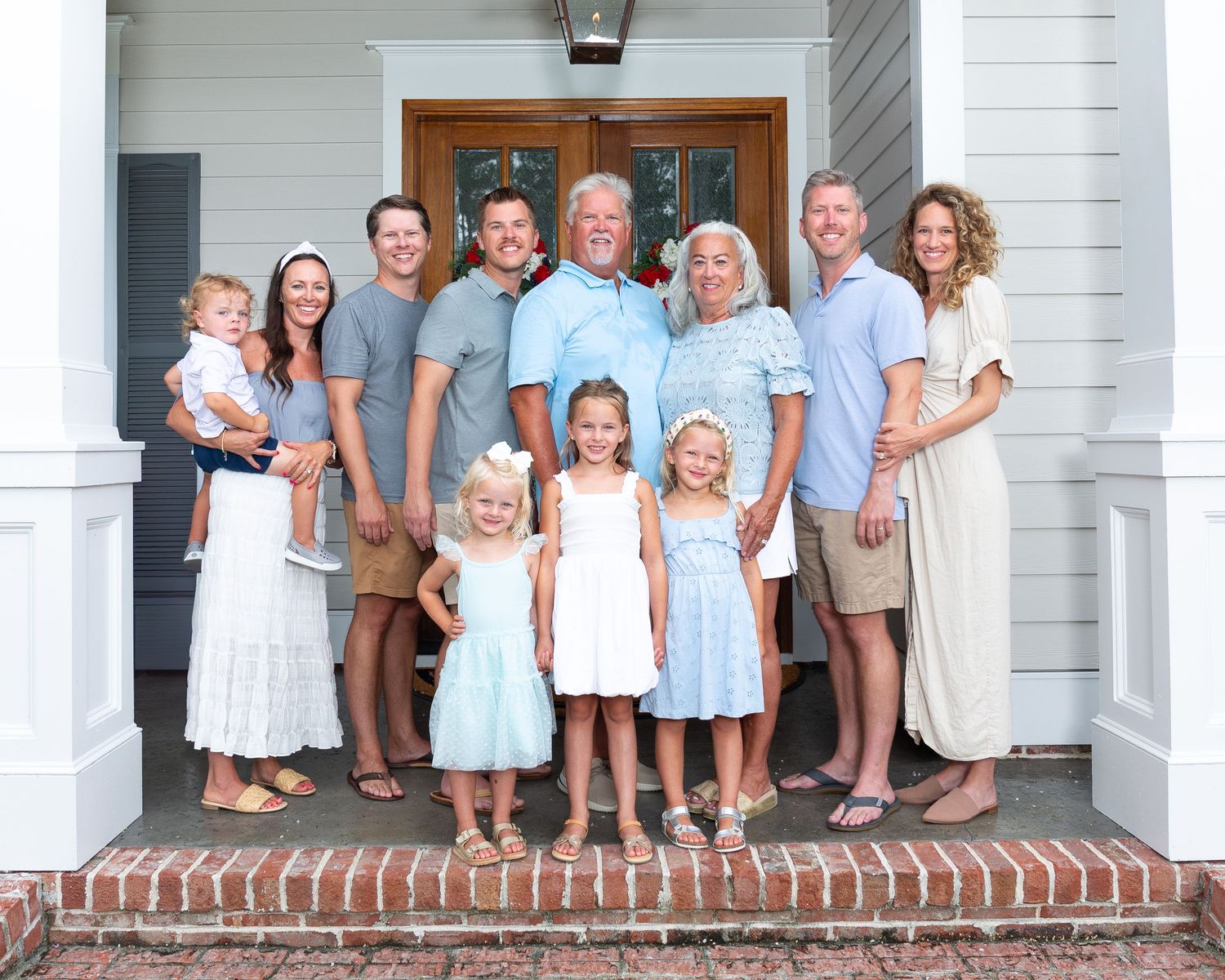 Large family group poses together on brick steps of a white house porch for a portrait.